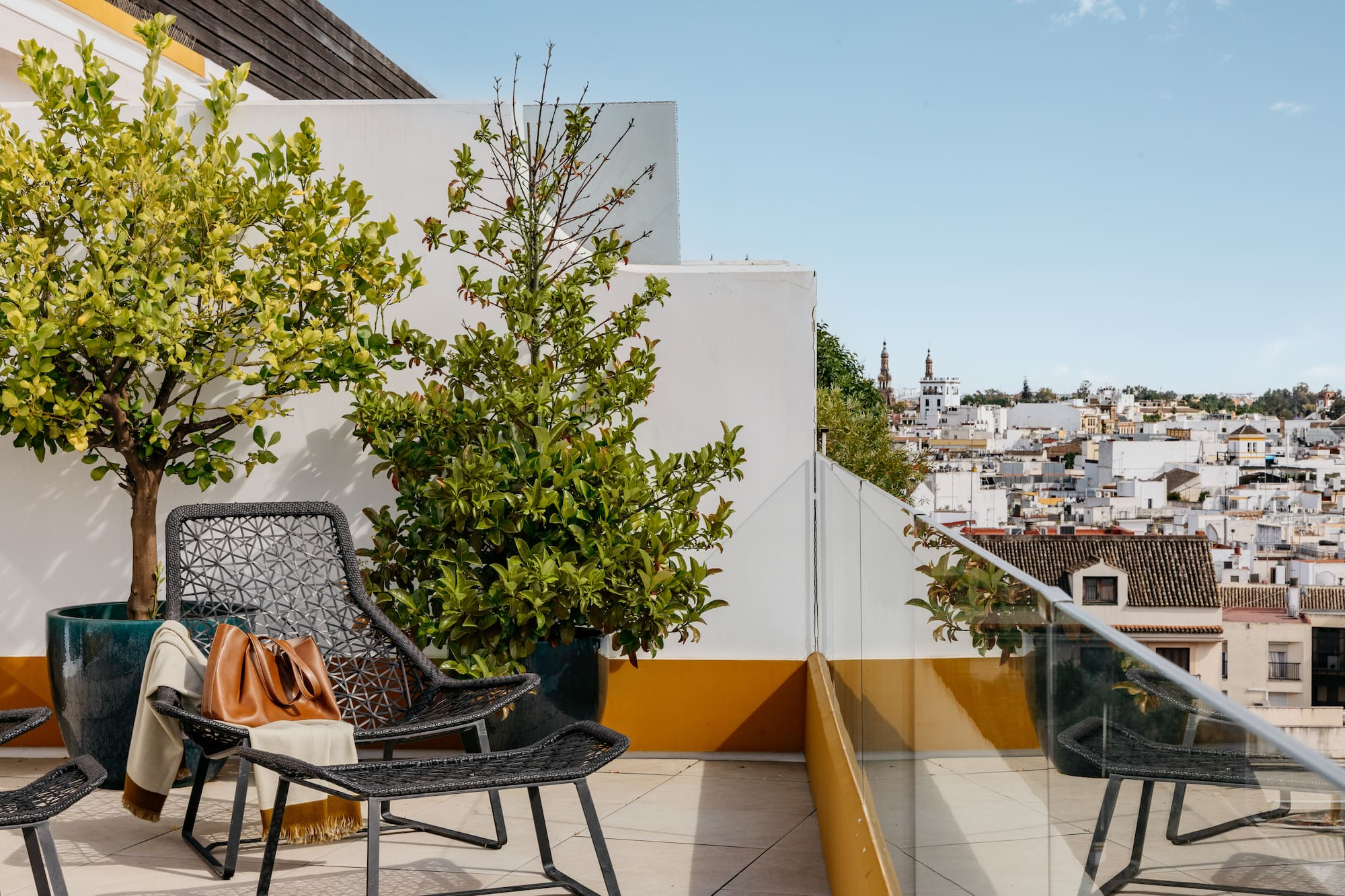 Terraza azotea con sillas, plantas y vista urbana mediterránea.