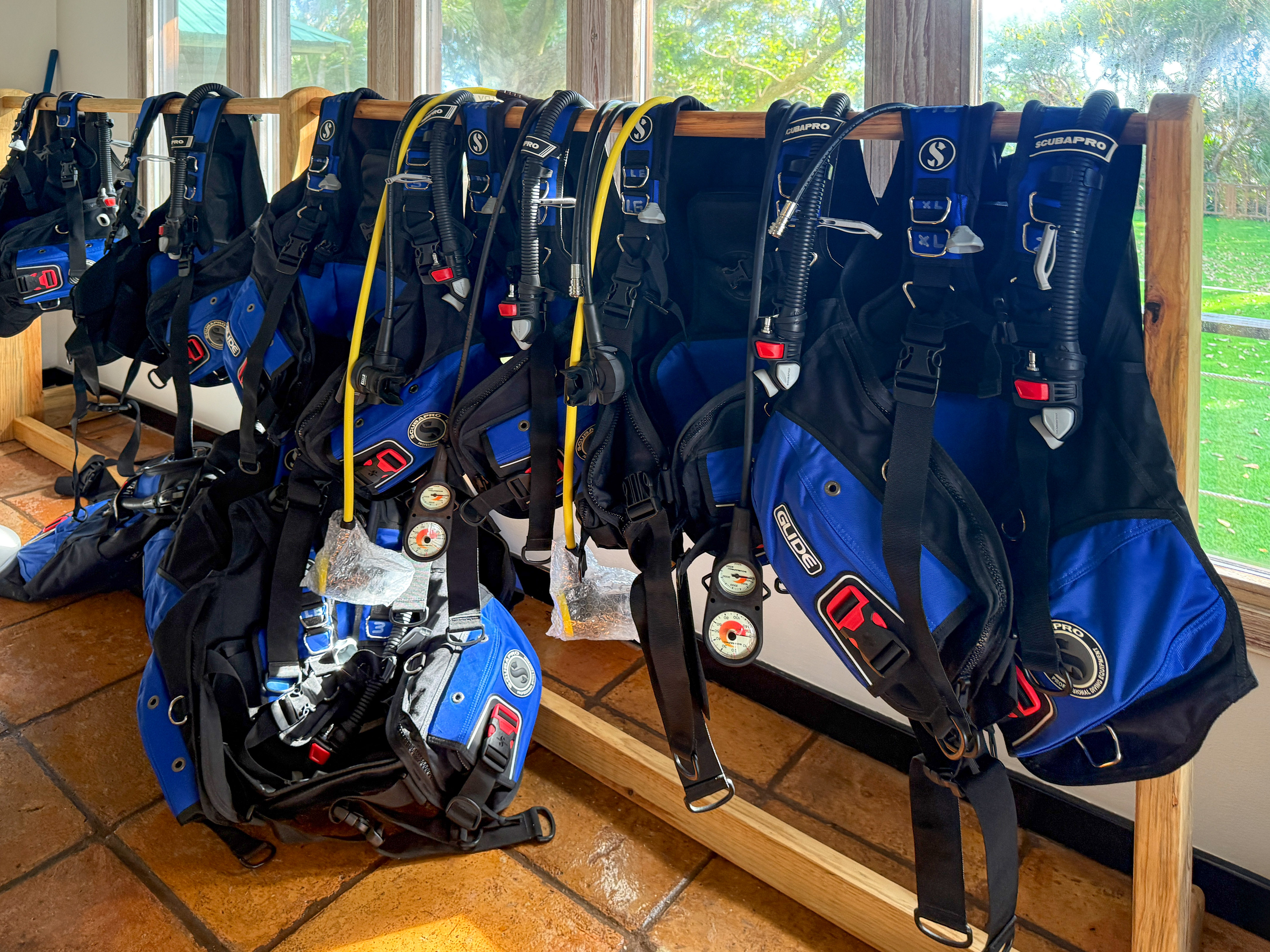 Blue and black Scubapro diving BCDs and regulators on a wooden rack.