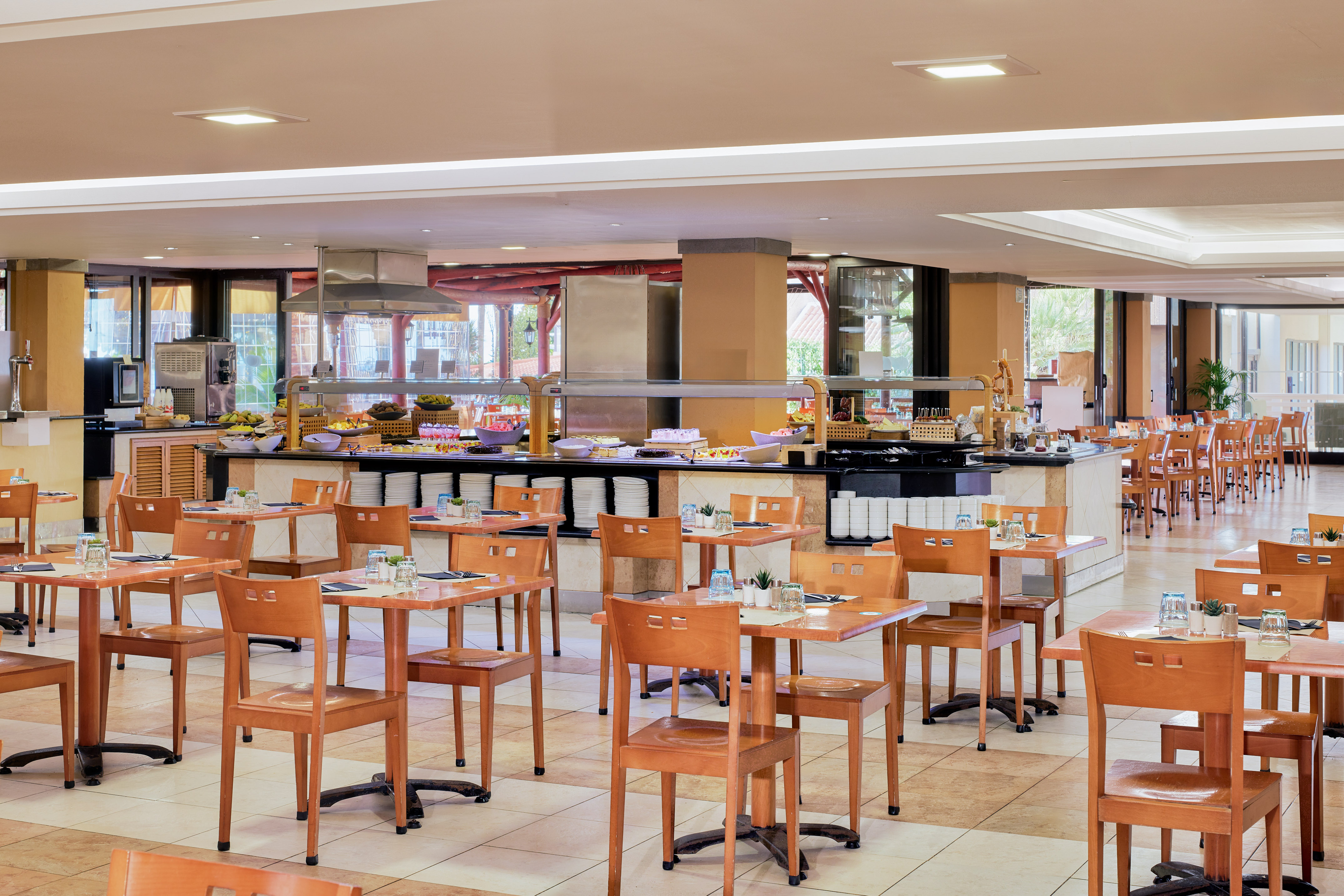Hotel buffet restaurant with food stations, wooden tables and chairs.