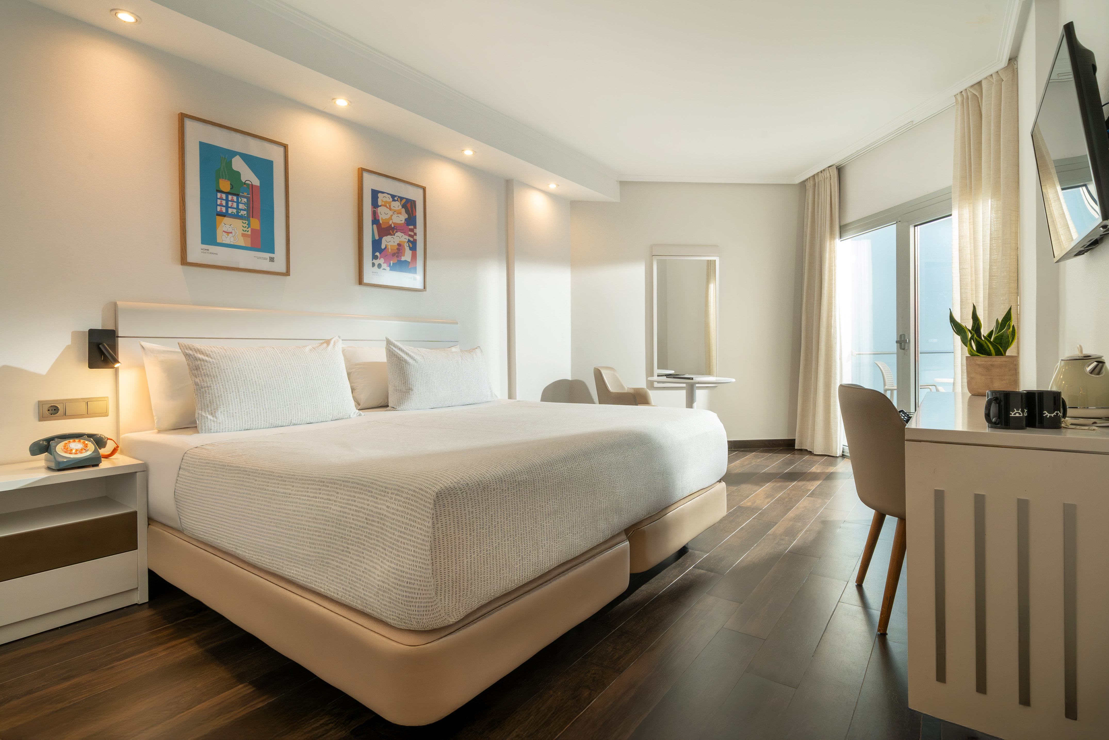 Modern hotel room with large bed, wooden floor, balcony, and desk area.
