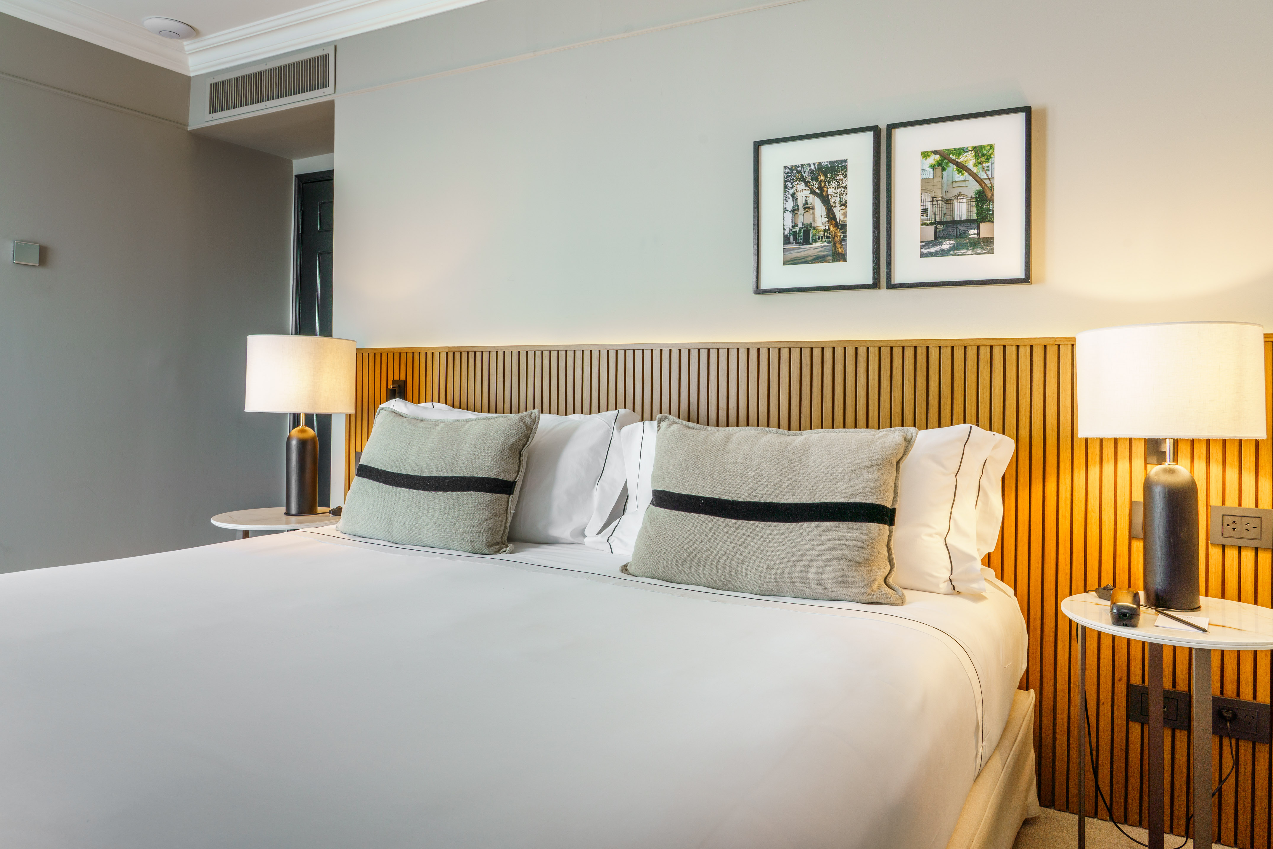 Modern hotel bedroom with king-size bed, slatted wood headboard, and two lamps.