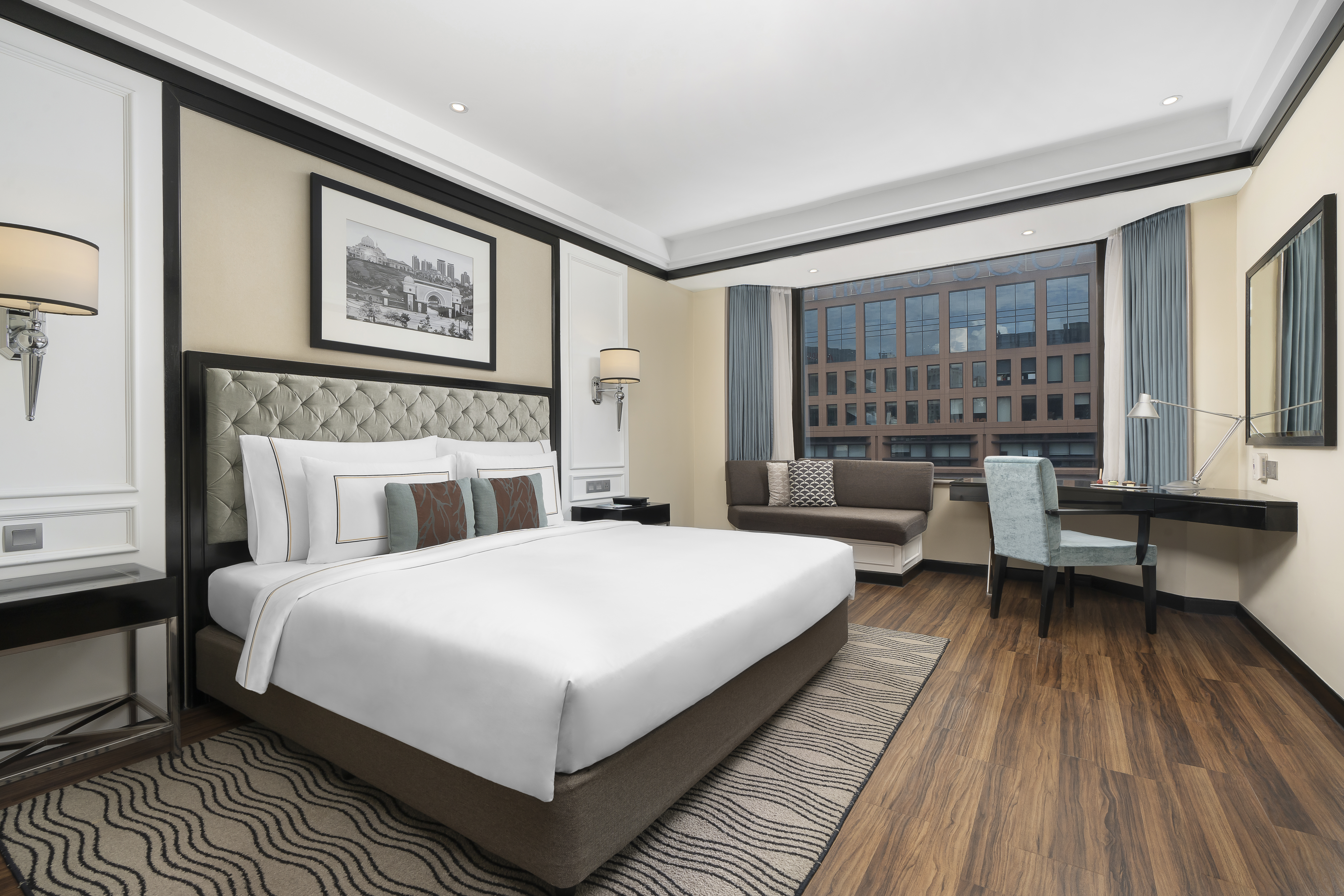 Modern hotel bedroom with king bed, desk, window sofa, and city view.