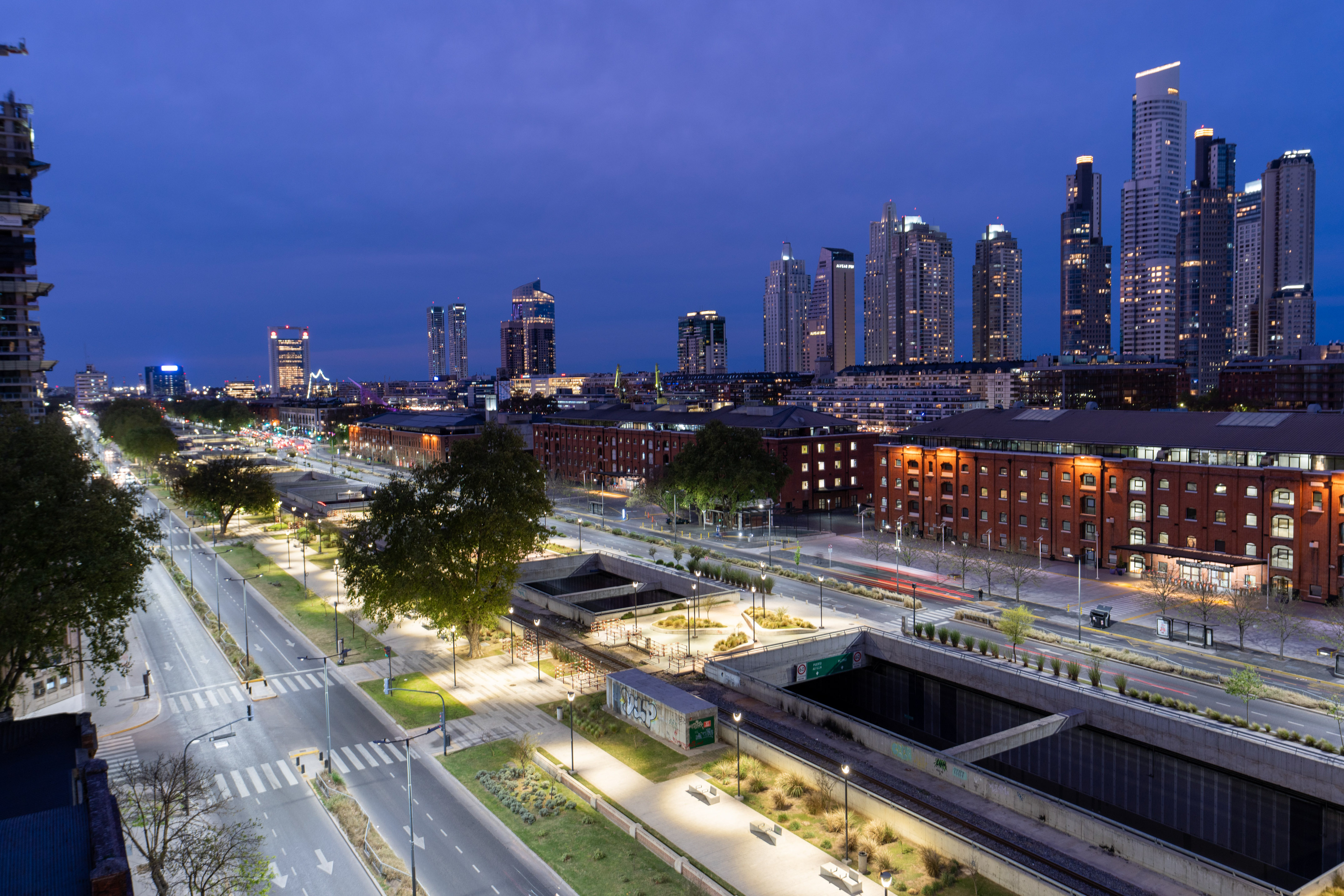 Urban night view: modern skyscrapers, historic buildings, lit roads, train tracks.