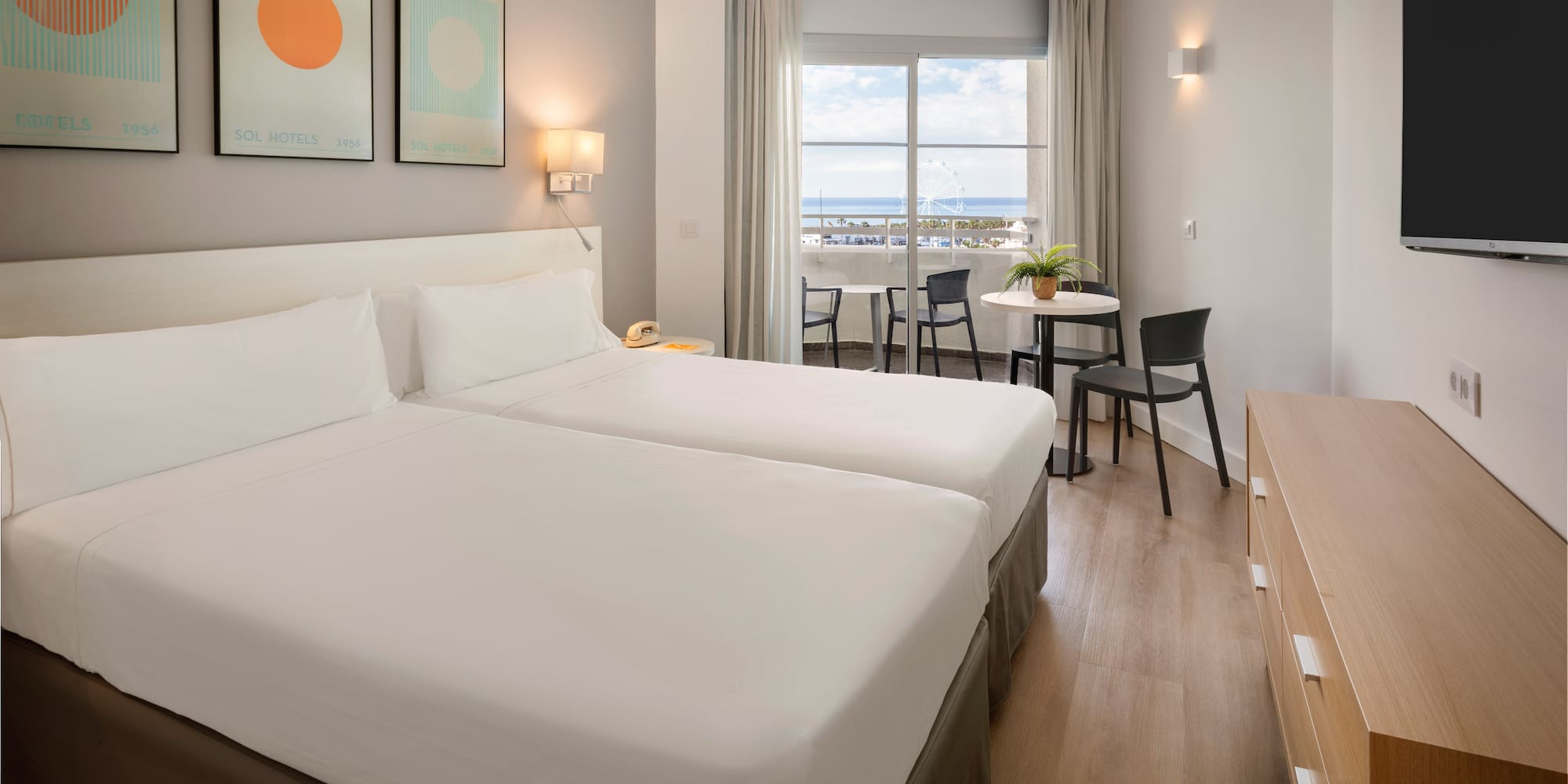 Modern hotel room with twin beds, balcony, and sea view.