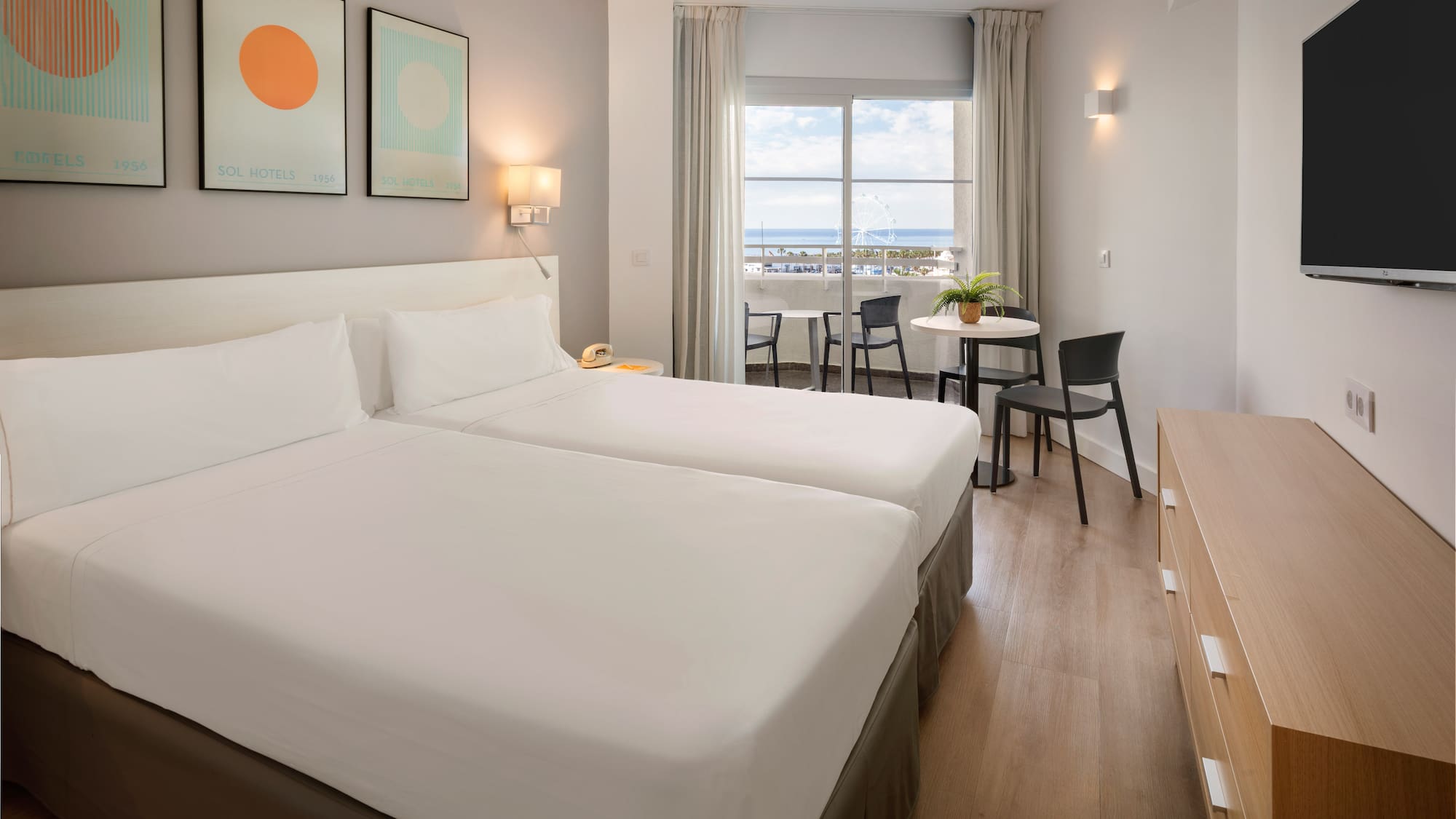 Modern hotel room with twin beds, balcony, and sea view.