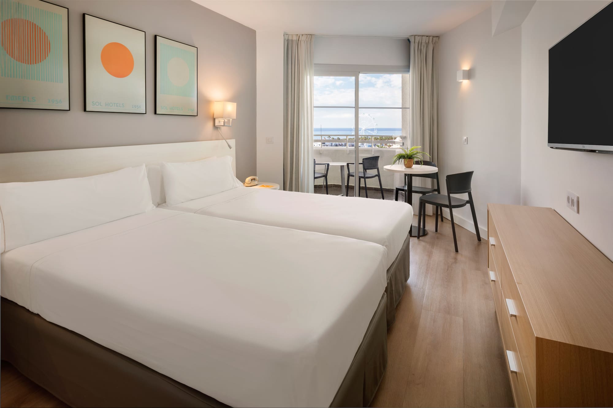 Modern hotel room with twin beds, balcony, and sea view.