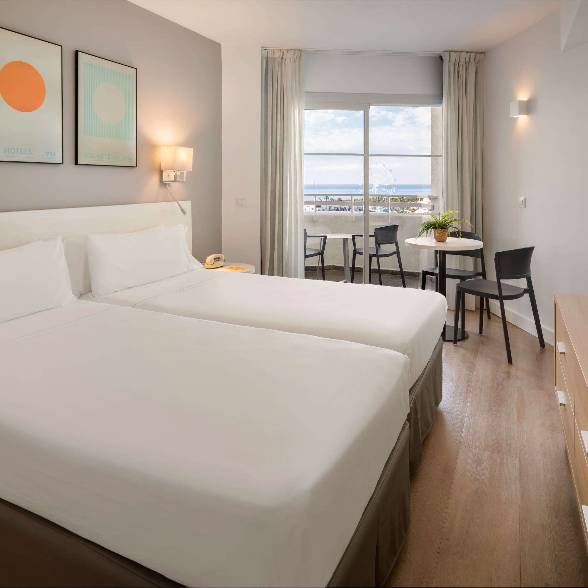 Modern hotel room with twin beds, balcony, and sea view.