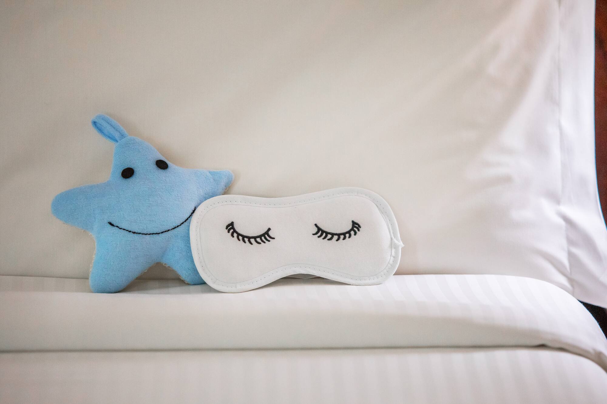 Blue star plush toy and white sleep mask with eyelashes on a bed.