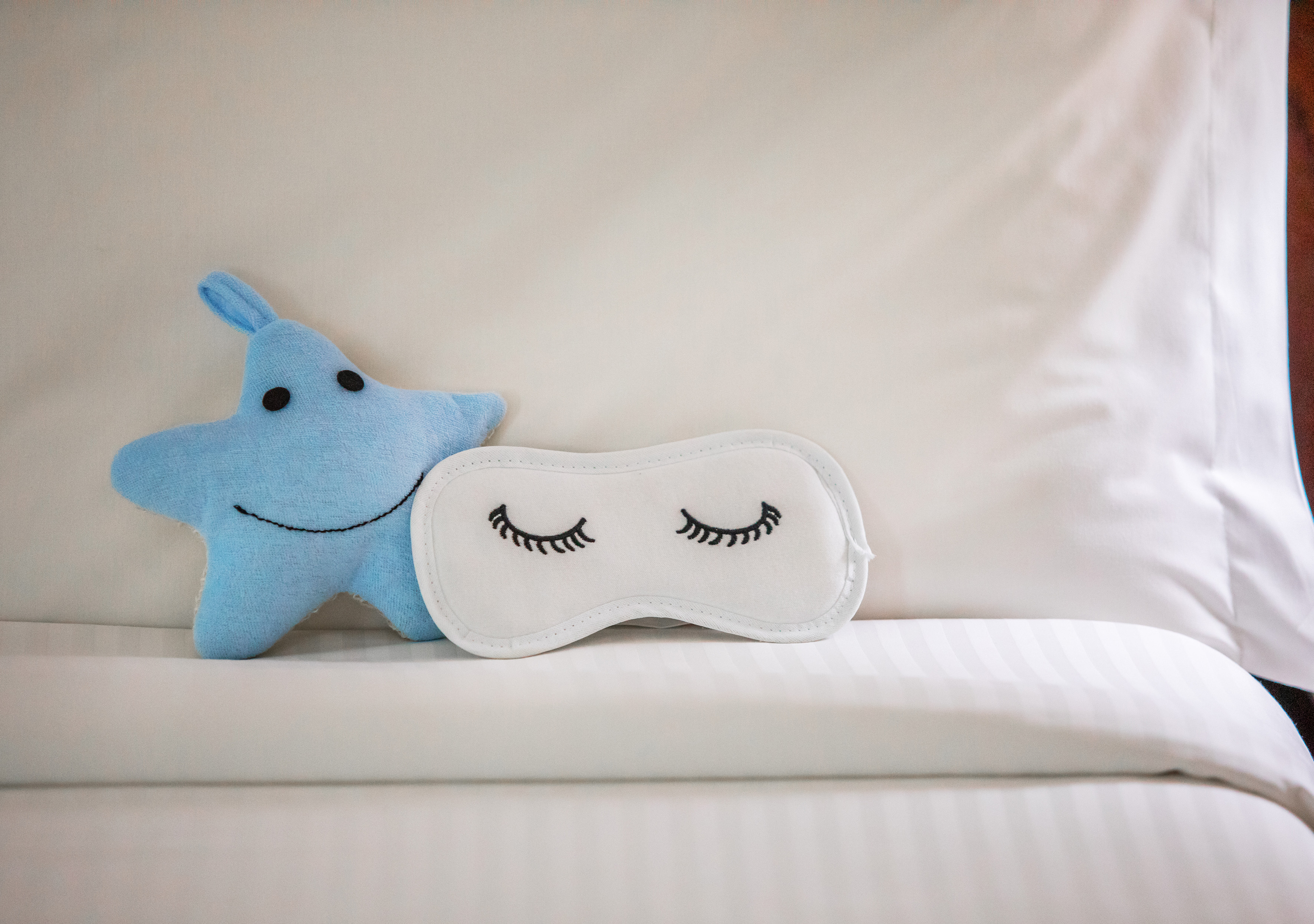 Blue star plush toy and white sleep mask with eyelashes on a bed.