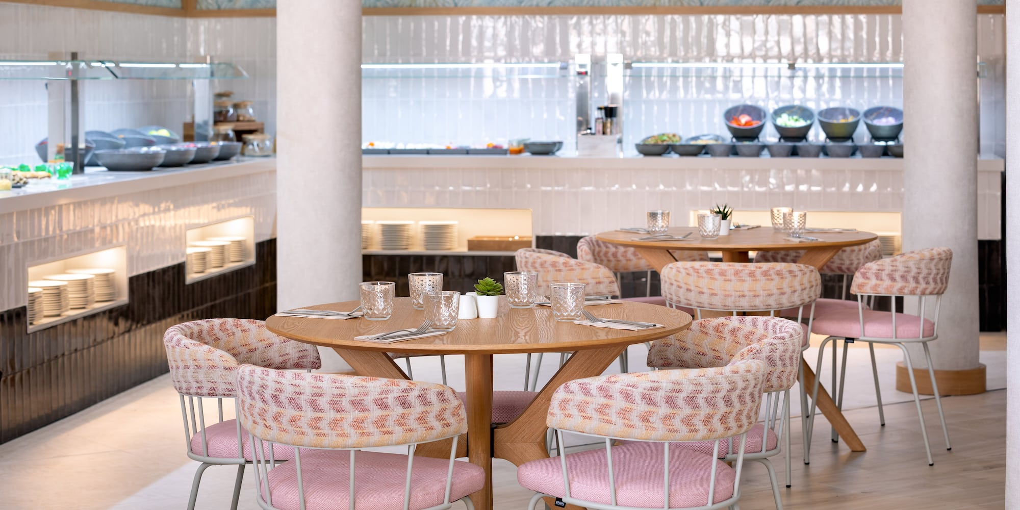 Modern restaurant interior featuring buffet, wooden tables, and pink chairs.