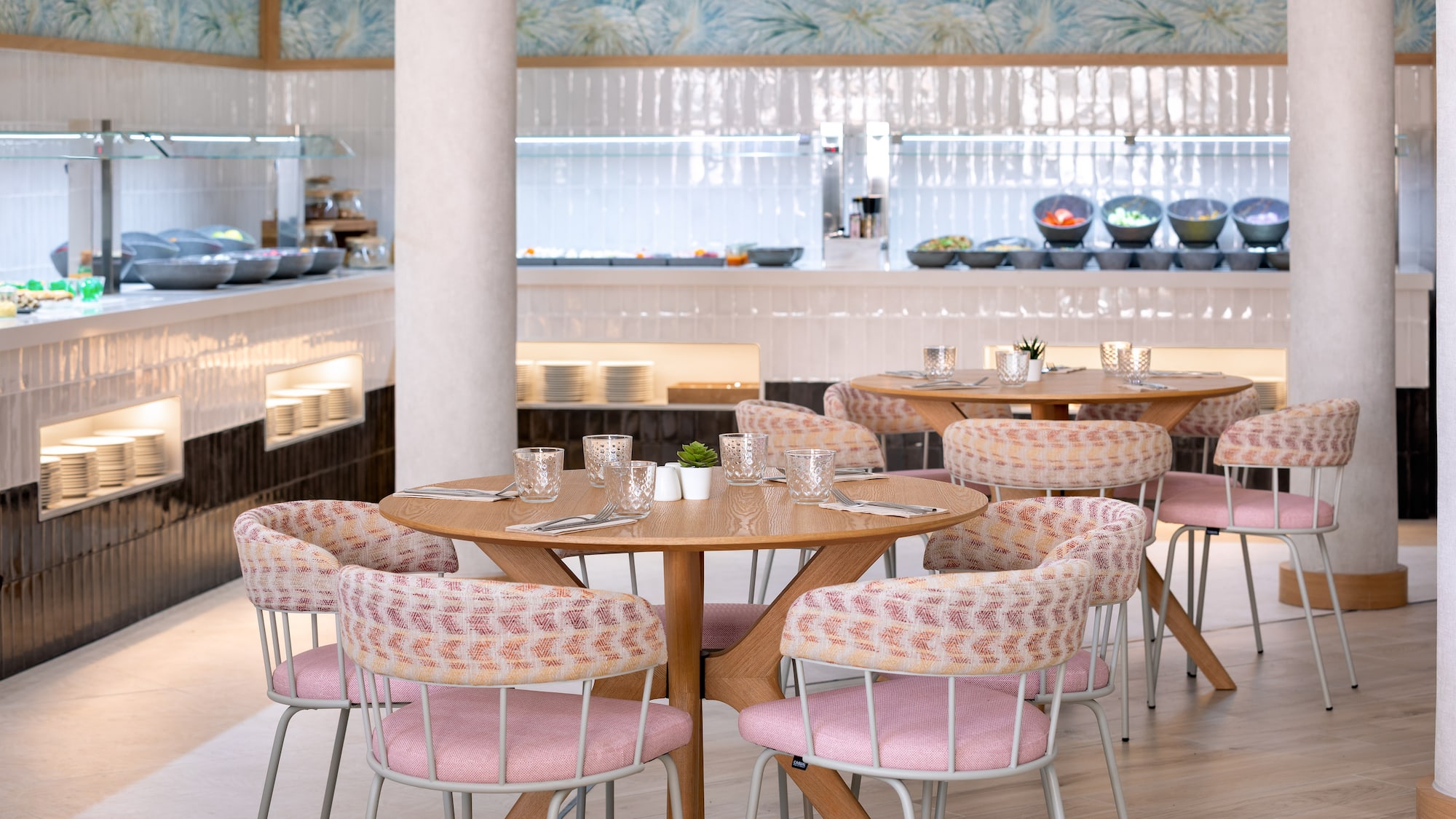Modern restaurant dining area with round tables, pink chairs, and a buffet station.