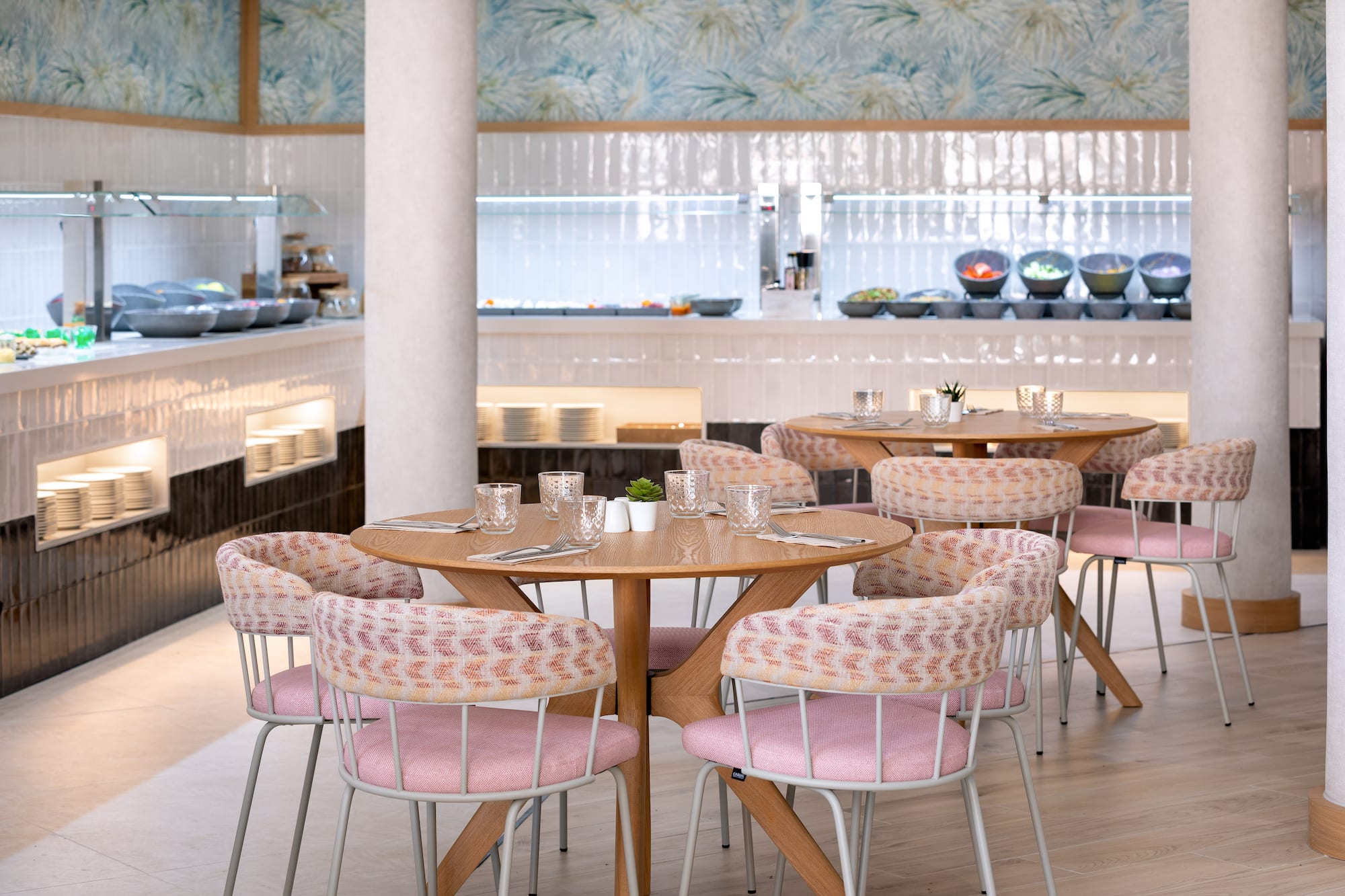 Modern restaurant interior featuring buffet, wooden tables, and pink chairs.