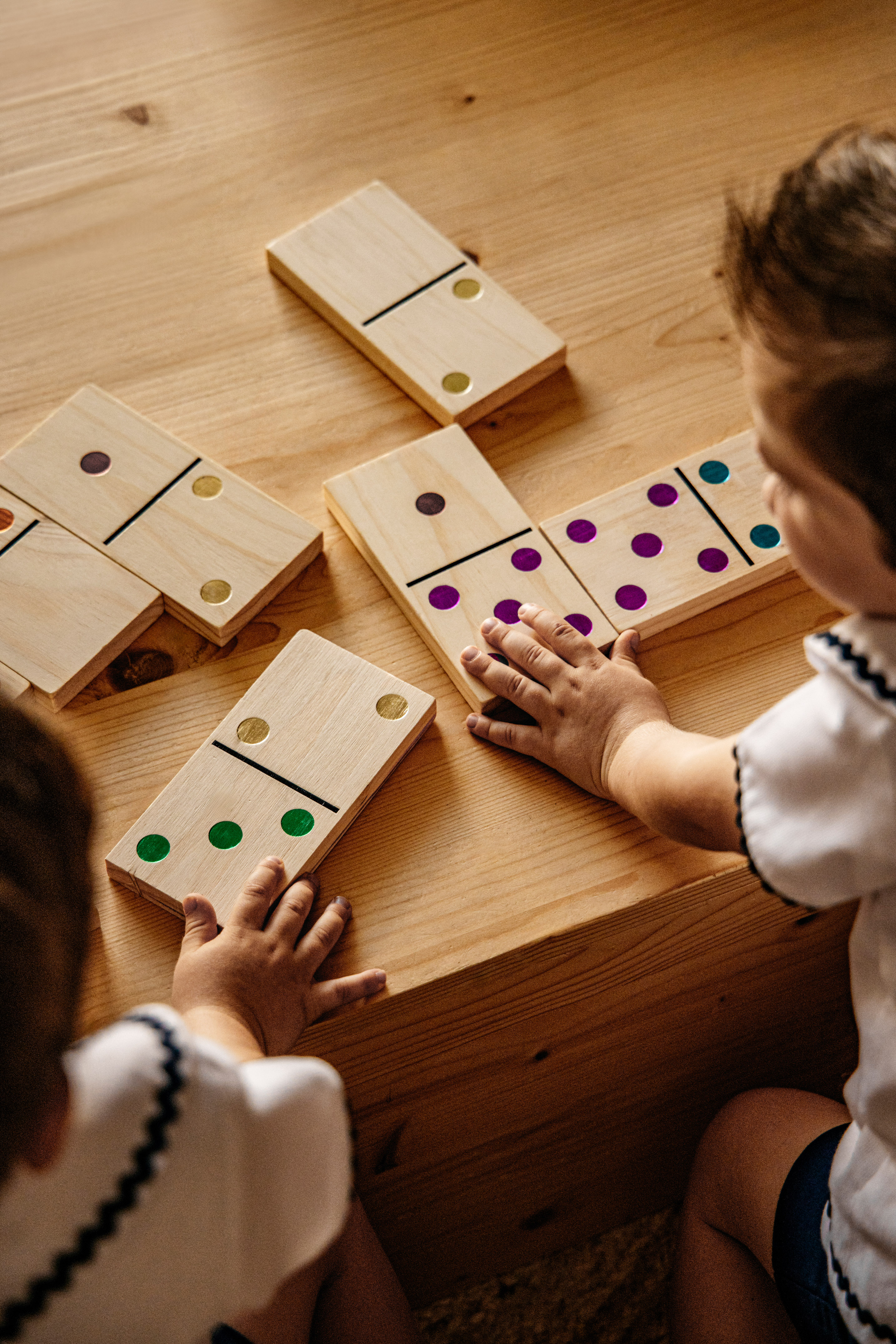 Children playing with colorful wooden dominoes on a wooden table.