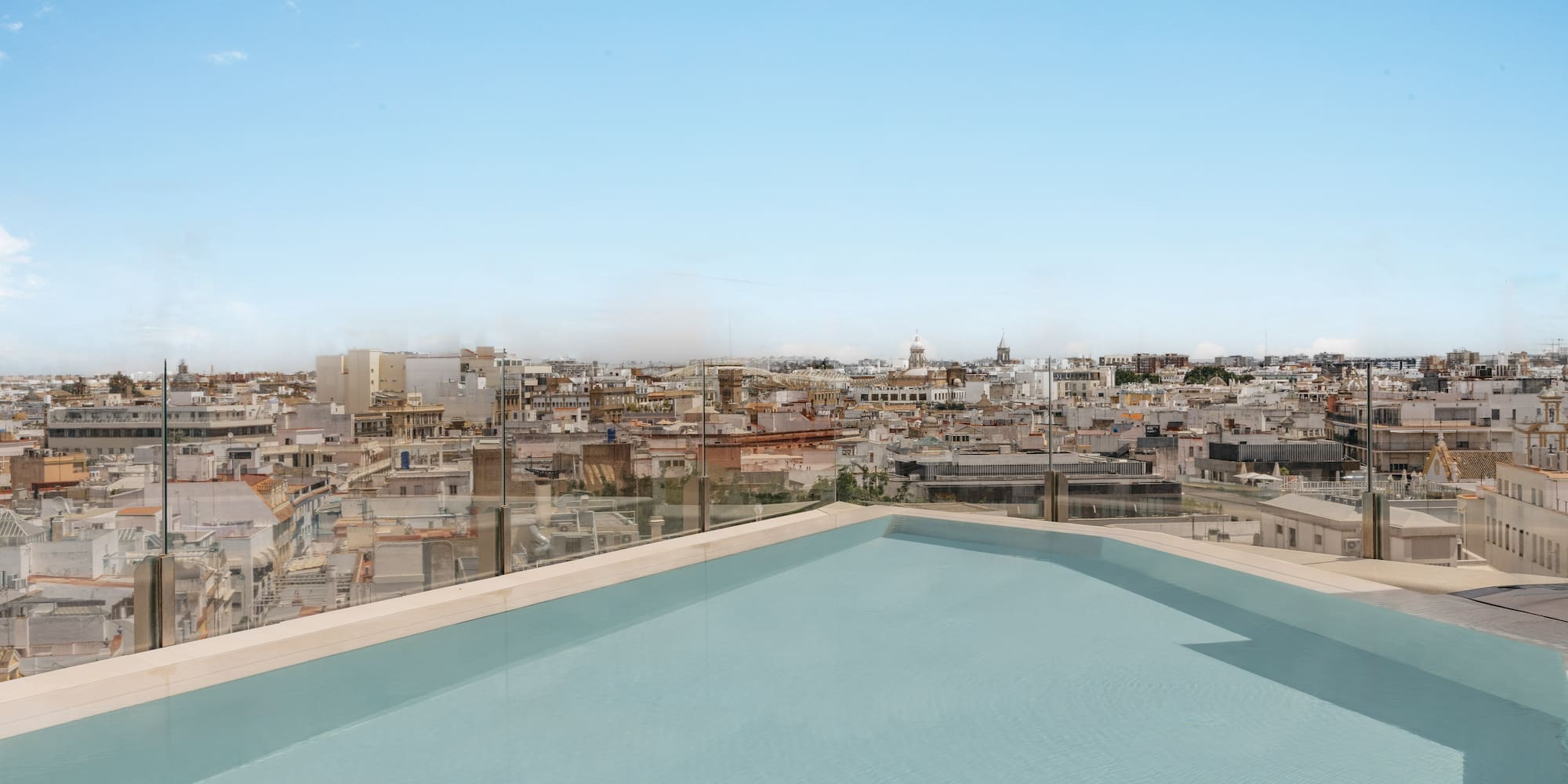 Piscina de azotea con vistas urbanas, arquitectura mediterránea y cielo azul.