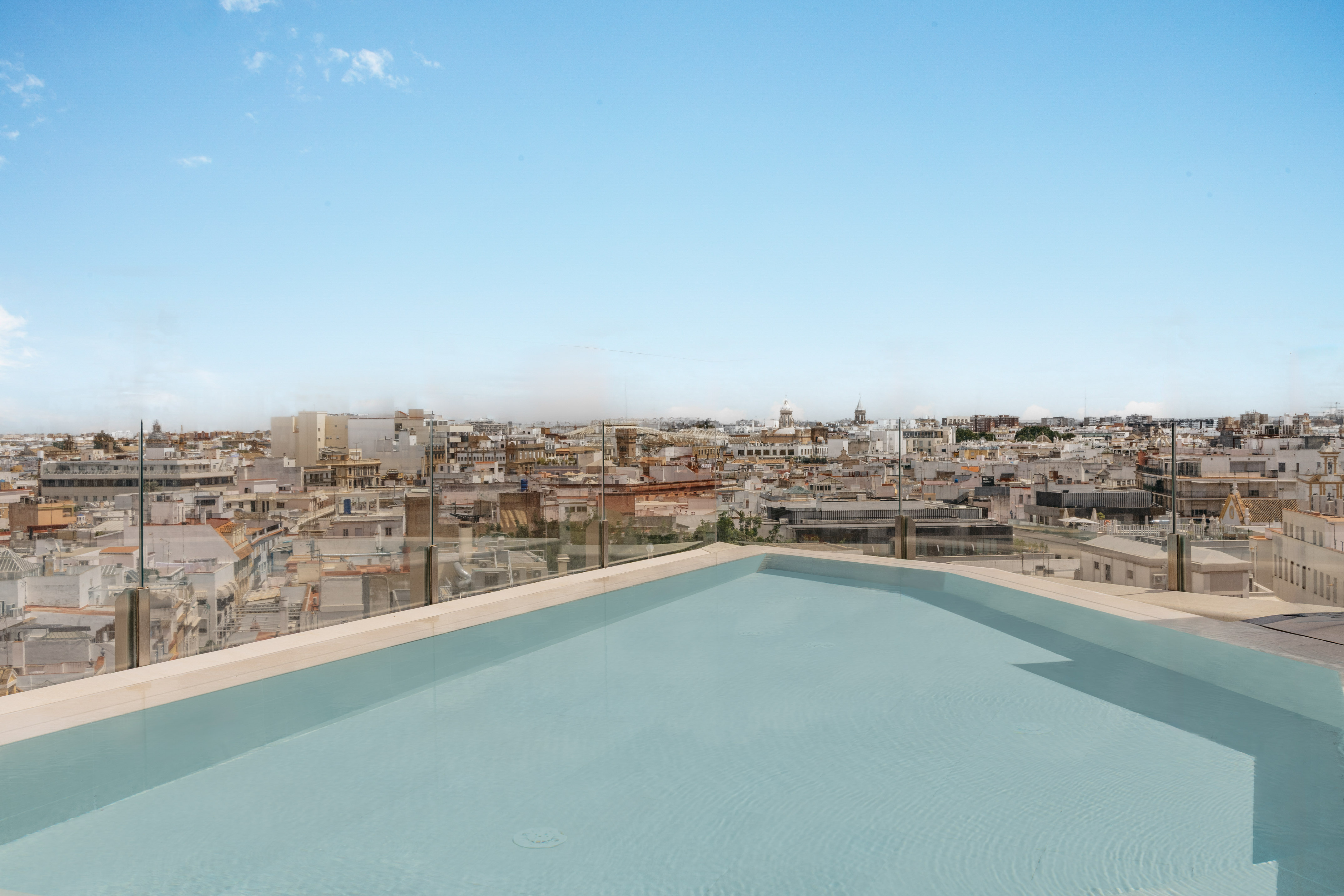 Luxury rooftop pool with city skyline view and blue sky.