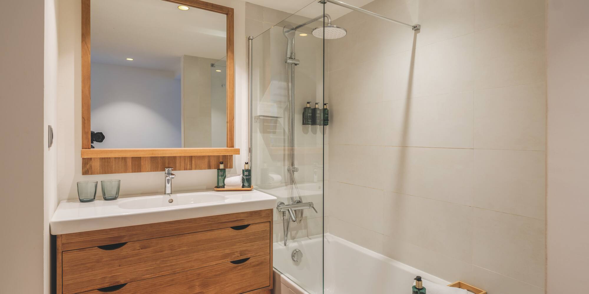 Contemporary bathroom with wooden vanity, mirror, bathtub, and glass shower.