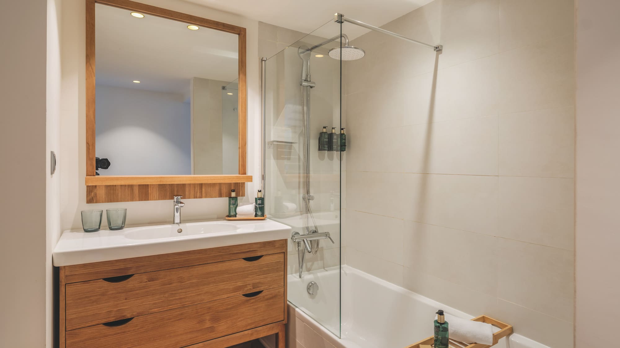 Contemporary bathroom with wooden vanity, mirror, bathtub, and glass shower.