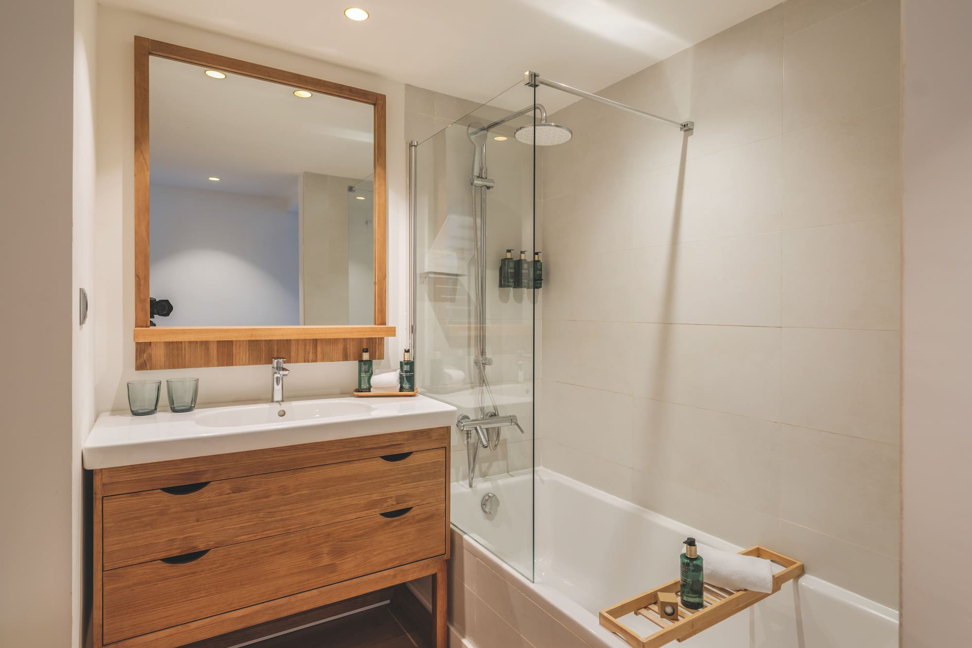 Contemporary bathroom with wooden vanity, mirror, bathtub, and glass shower.