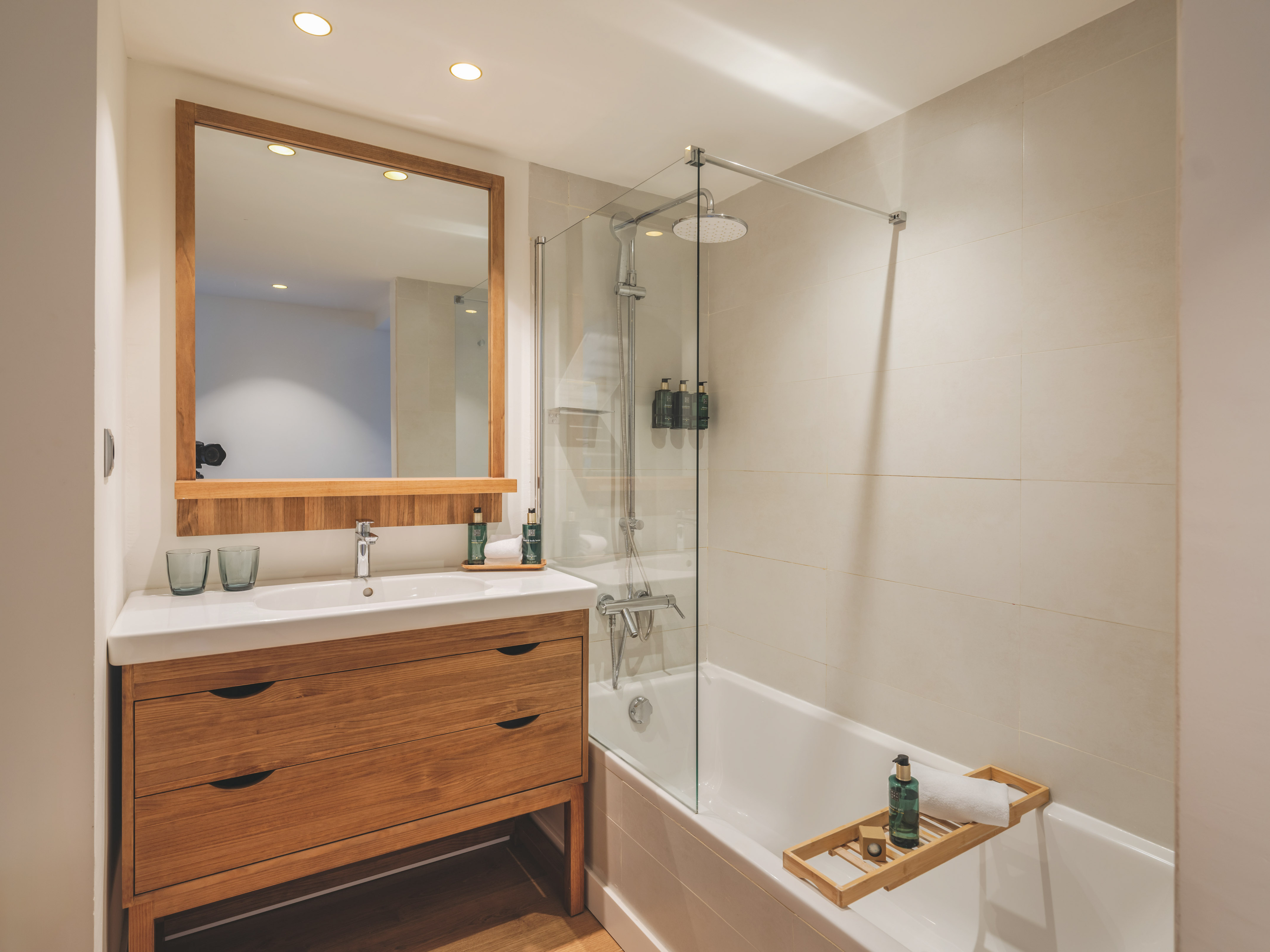 Contemporary bathroom with wooden vanity, mirror, bathtub, and glass shower.