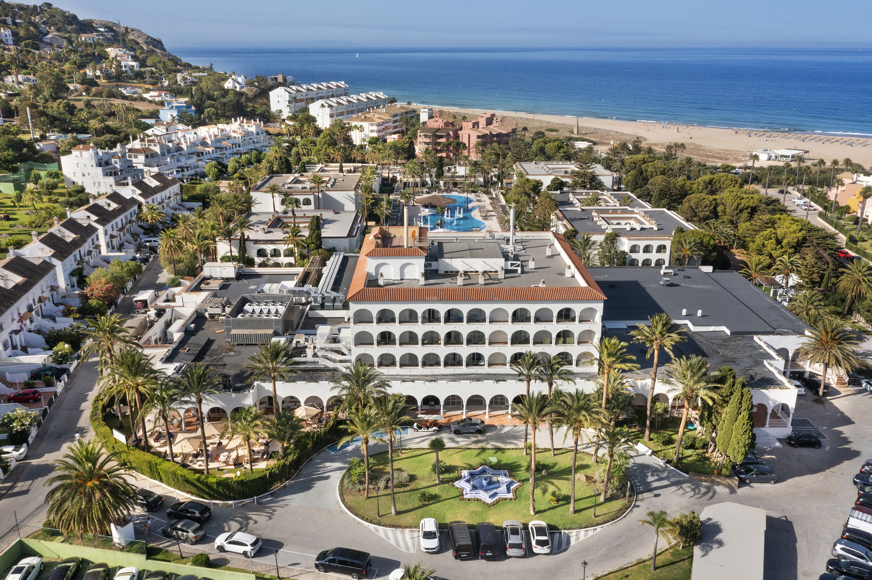 Aerial view of beachfront resort hotel, pool, beach, ocean, palm trees.