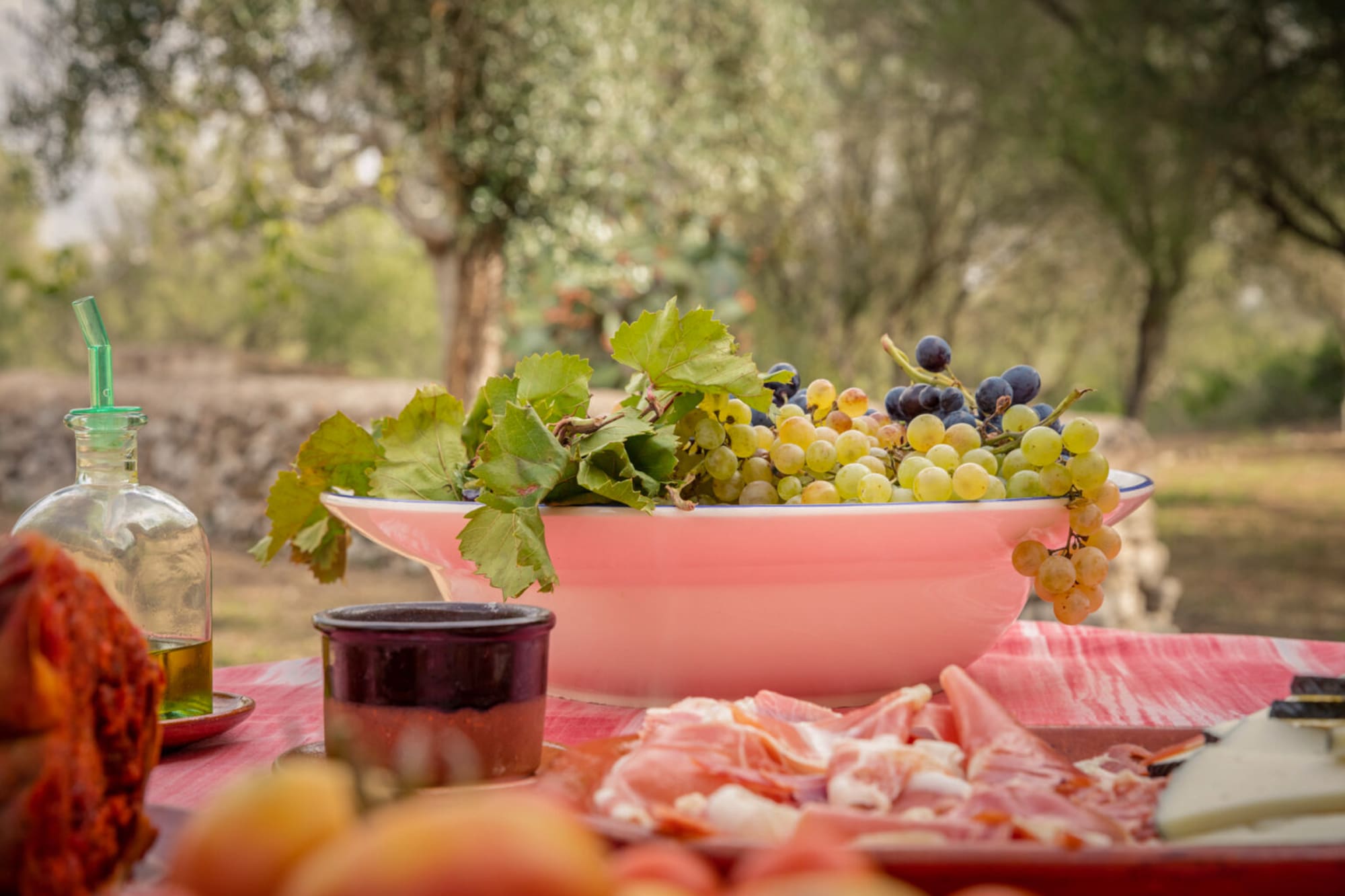 Uvas frescas, aceite de oliva, jamón y queso en mesa rústica al aire libre.