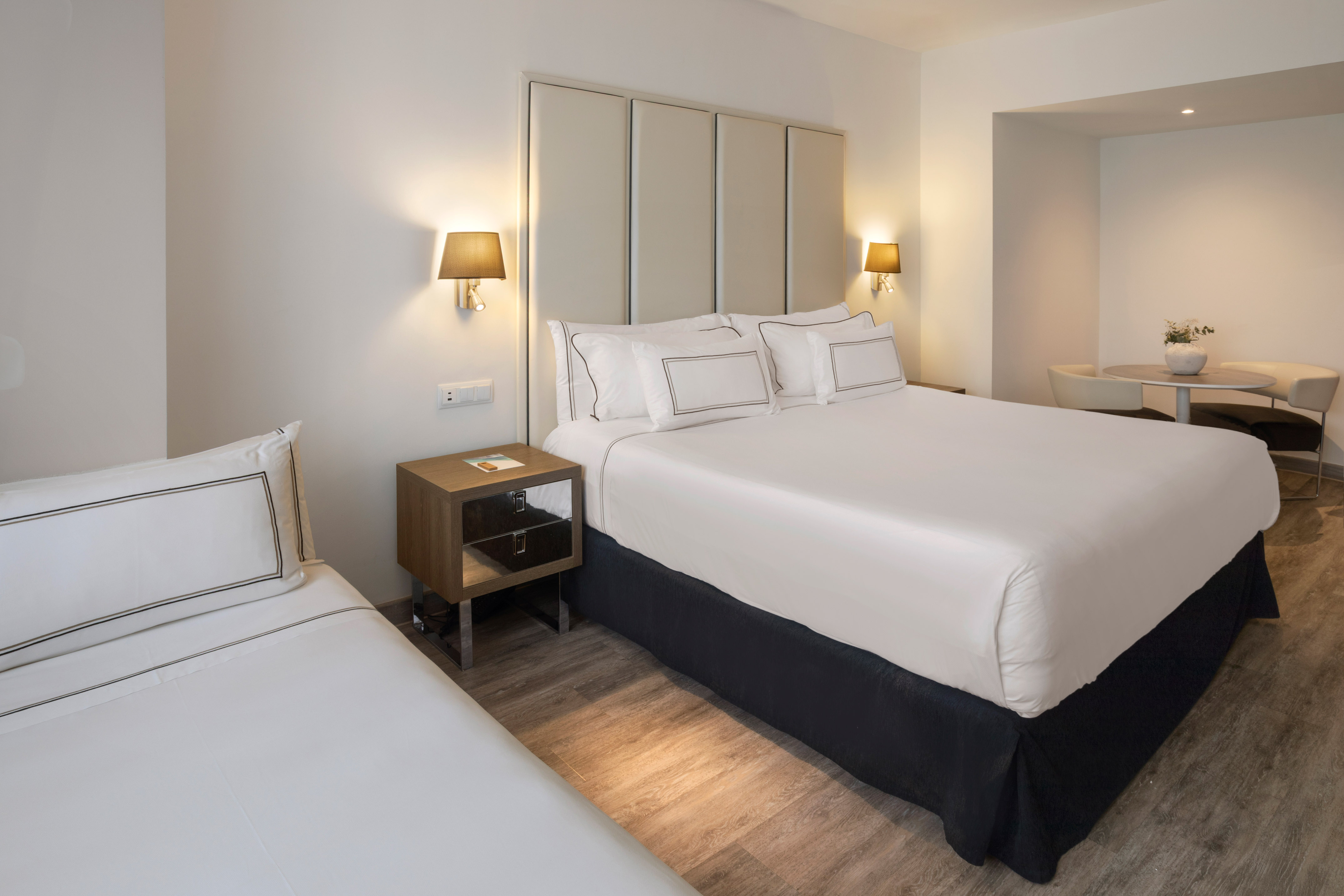 Modern hotel room with king bed, twin bed, nightstand, and small seating area.