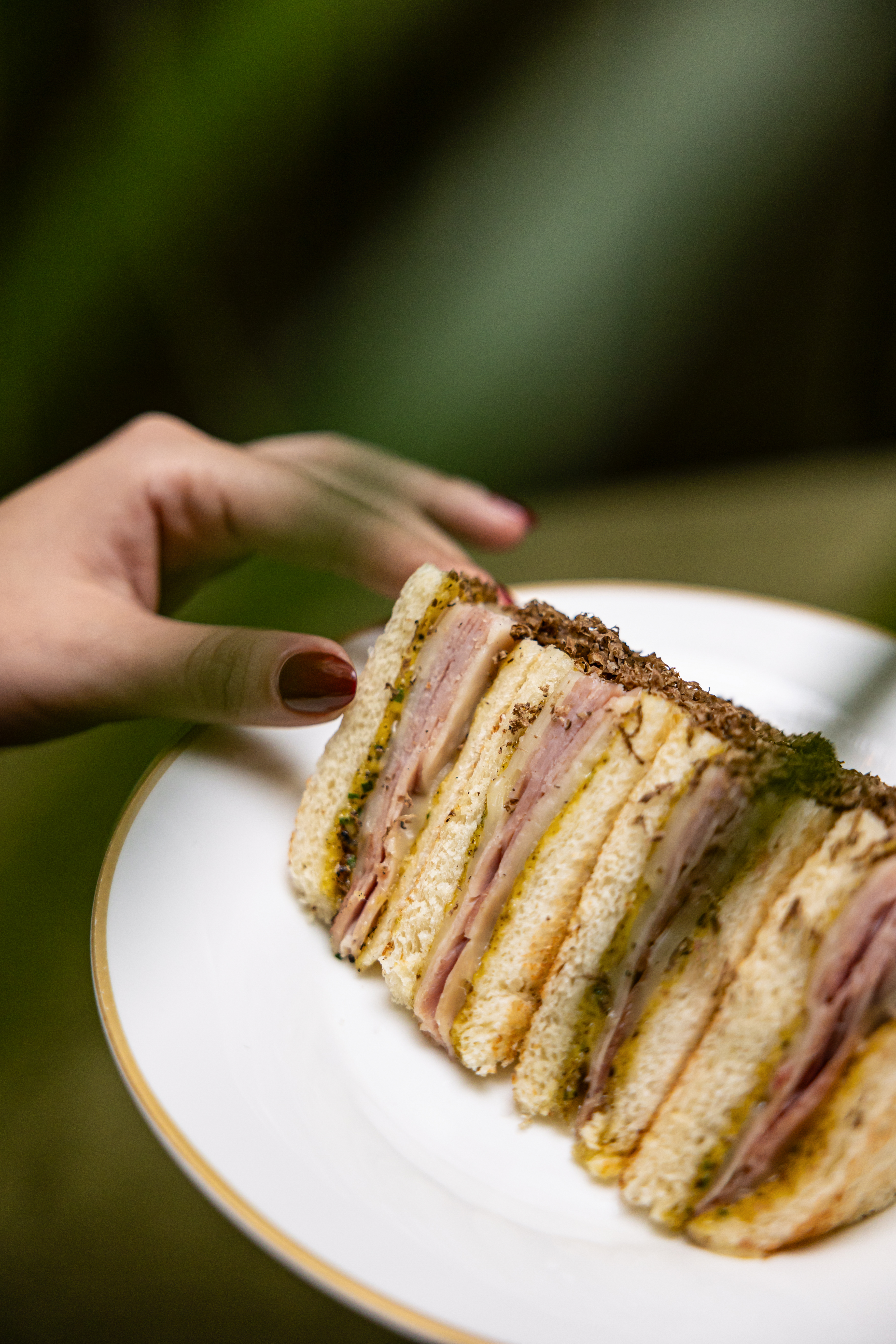 Truffle club sandwich with ham, cheese, pesto, on a white plate, held by hand.