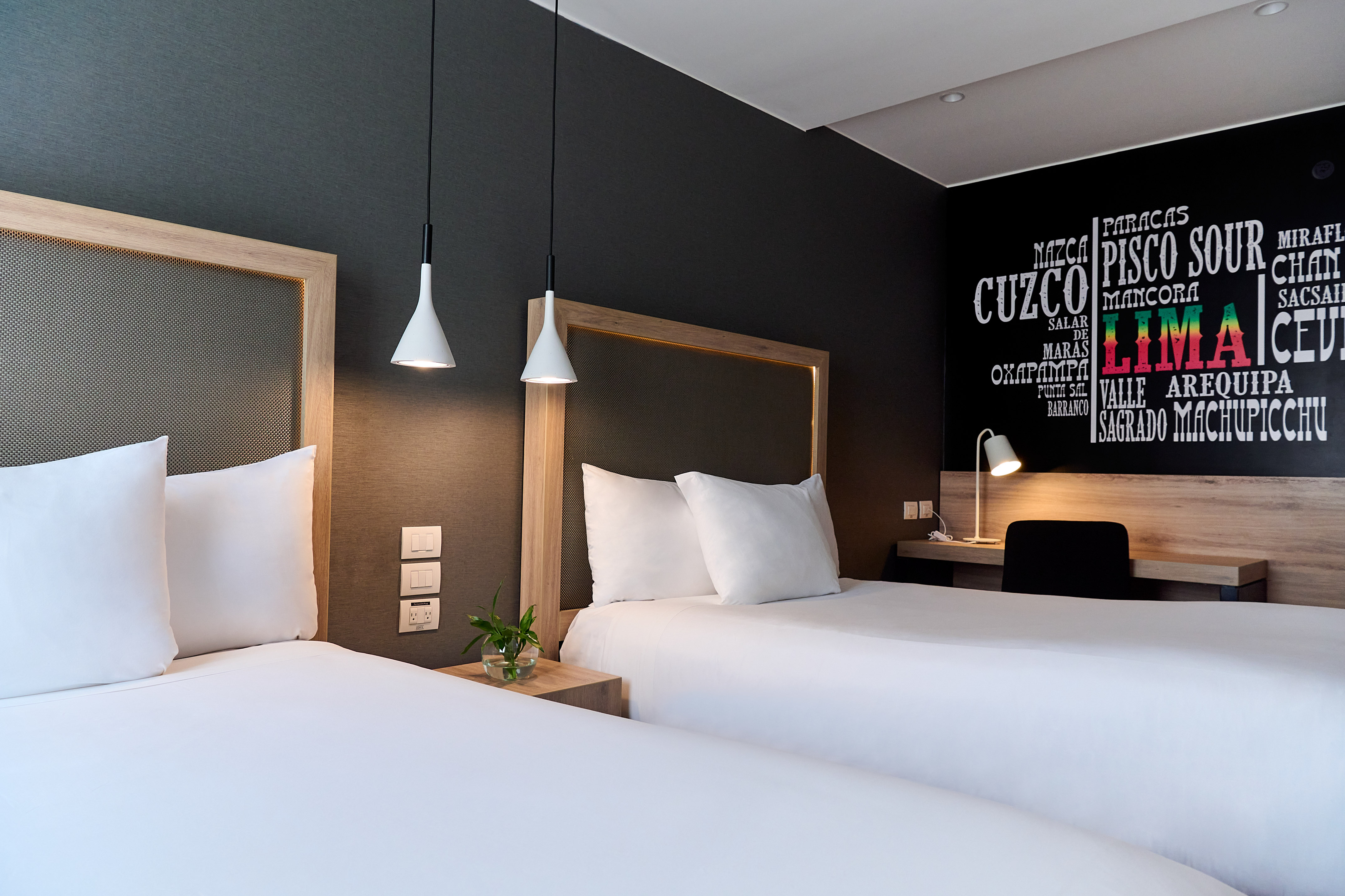 Modern hotel guest room with two beds and Peruvian-themed wall art.