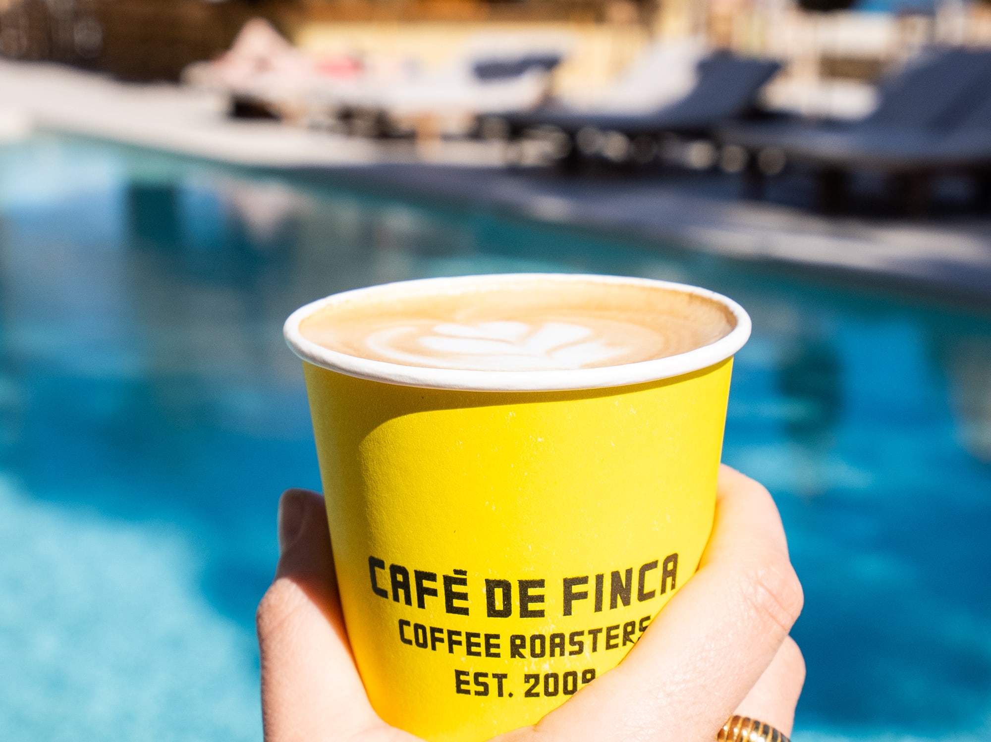 a hand holding a cup of coffee by a pool