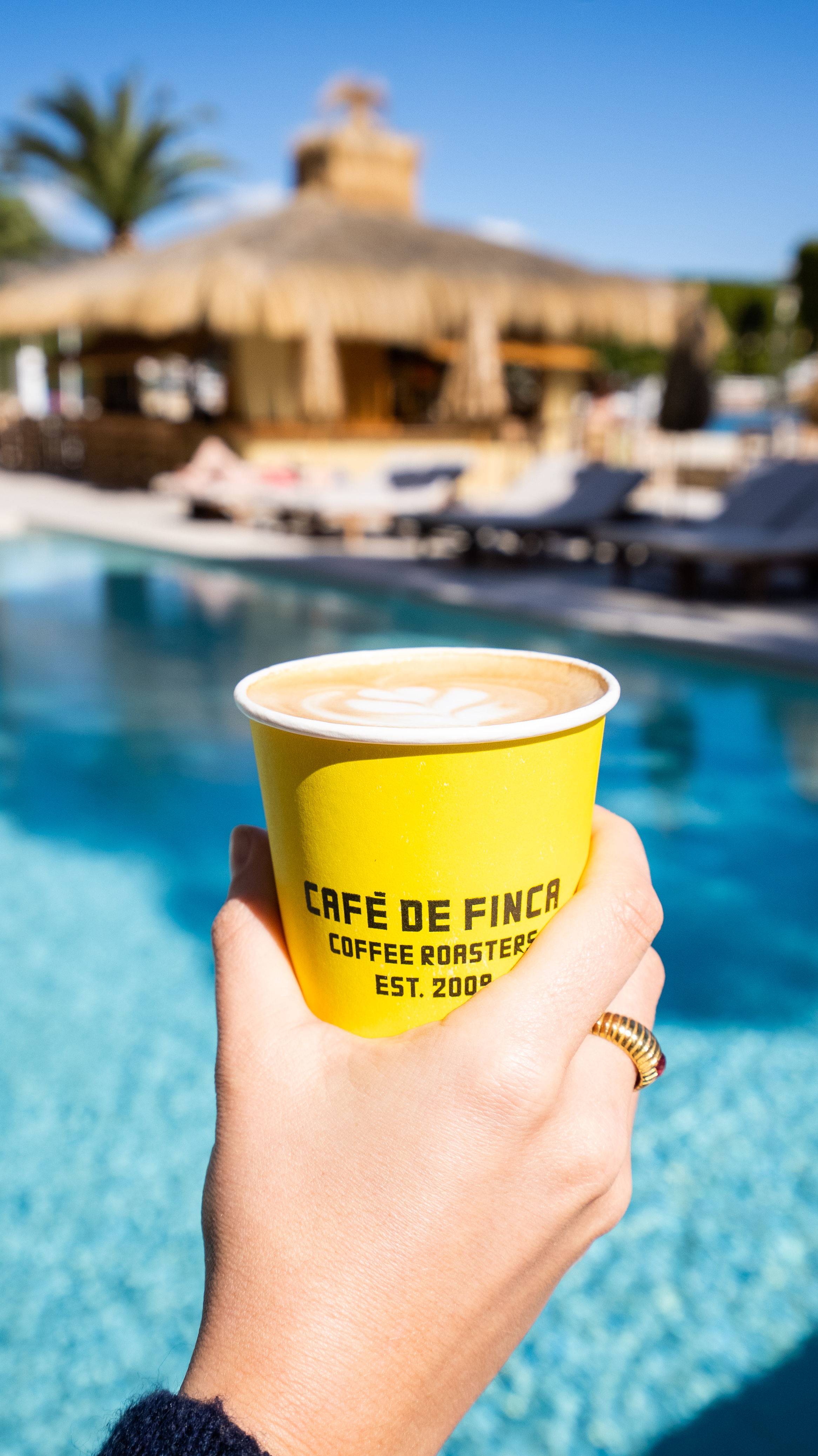 Yellow "Café de Finca" coffee held over a blue swimming pool on a sunny day.