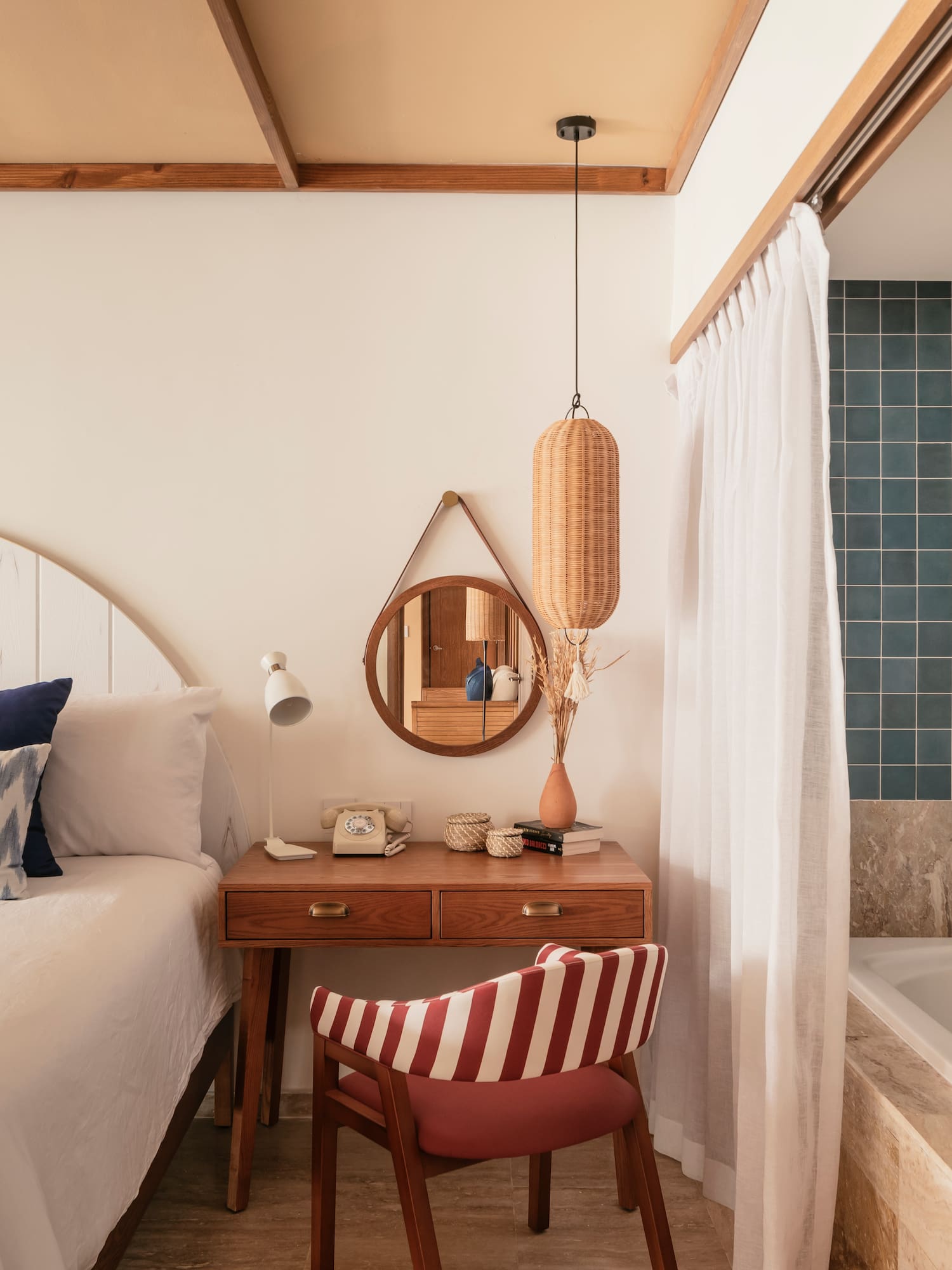 Hotel bedroom with white bed, wooden desk, and bathroom featuring tub, teal tiles.