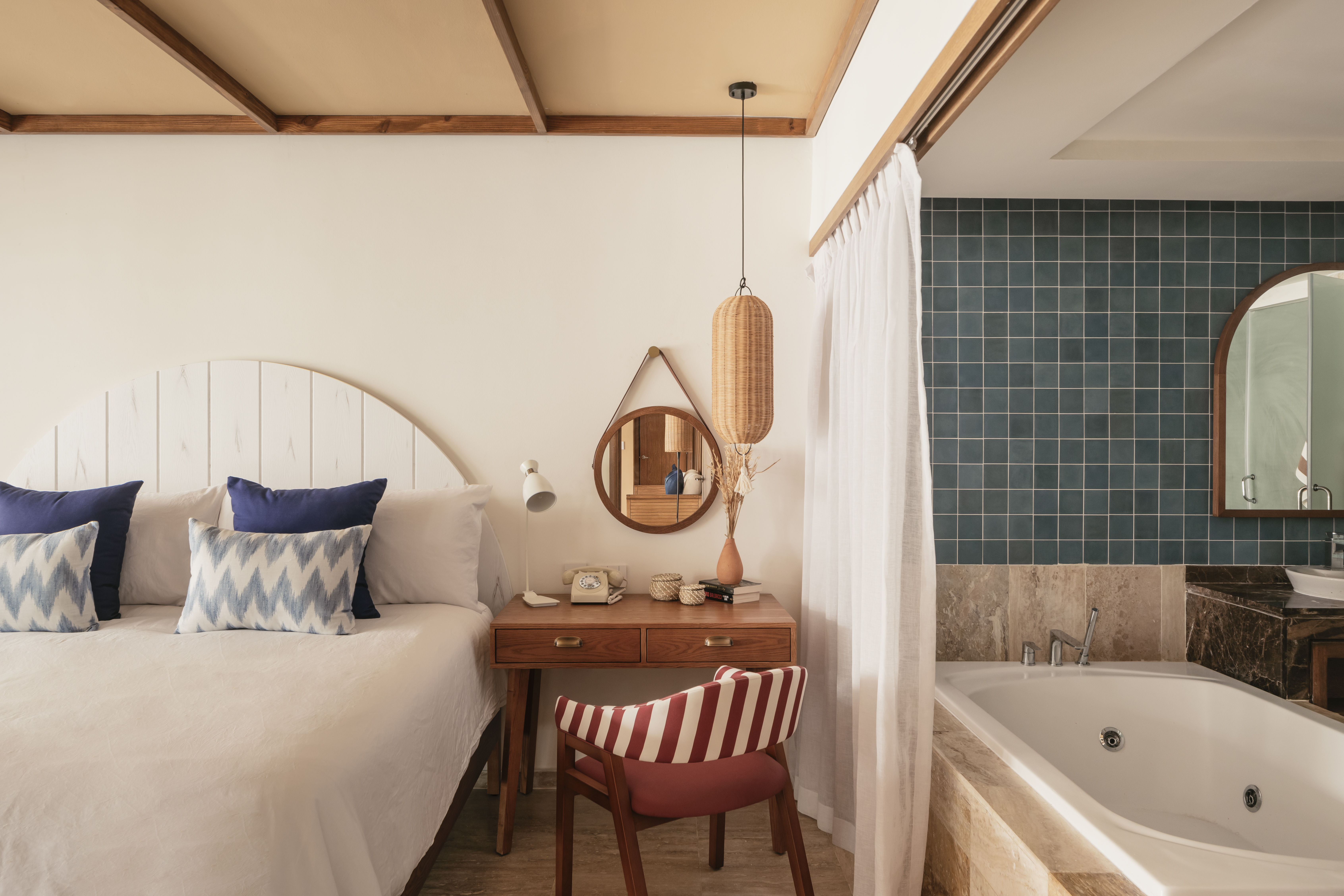 Hotel bedroom with white bed, wooden desk, and bathroom featuring tub, teal tiles.