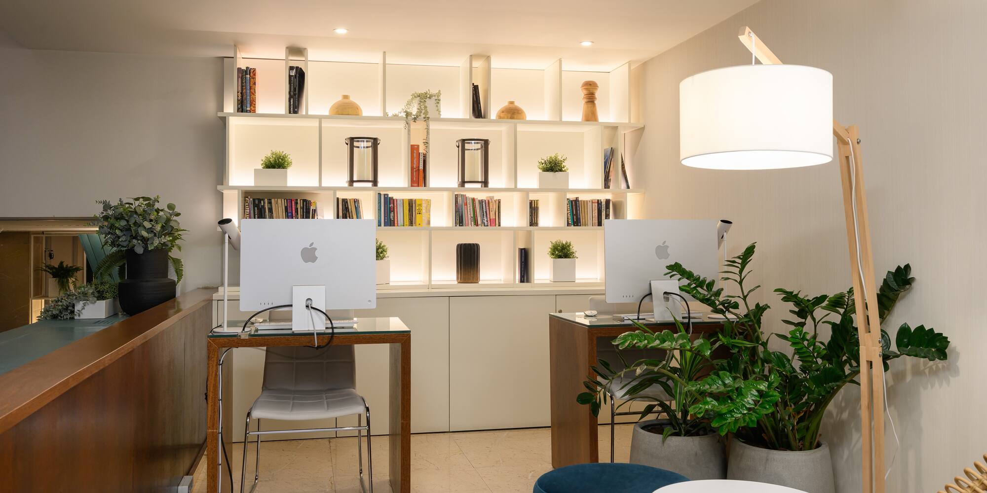 a room with a computer and shelves with books and plants