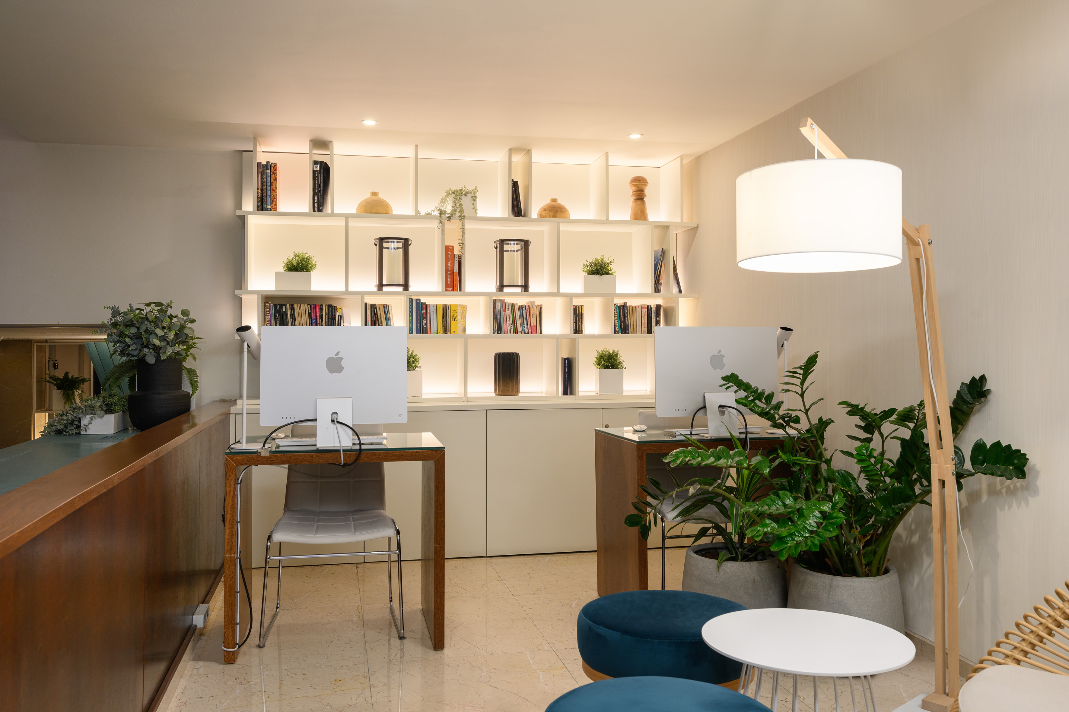 Modern coworking space with iMacs, illuminated bookshelves, and green plants.