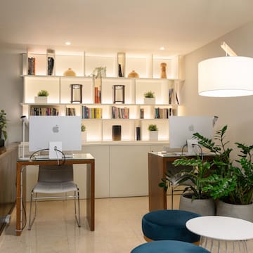 a room with a computer and shelves with books and plants