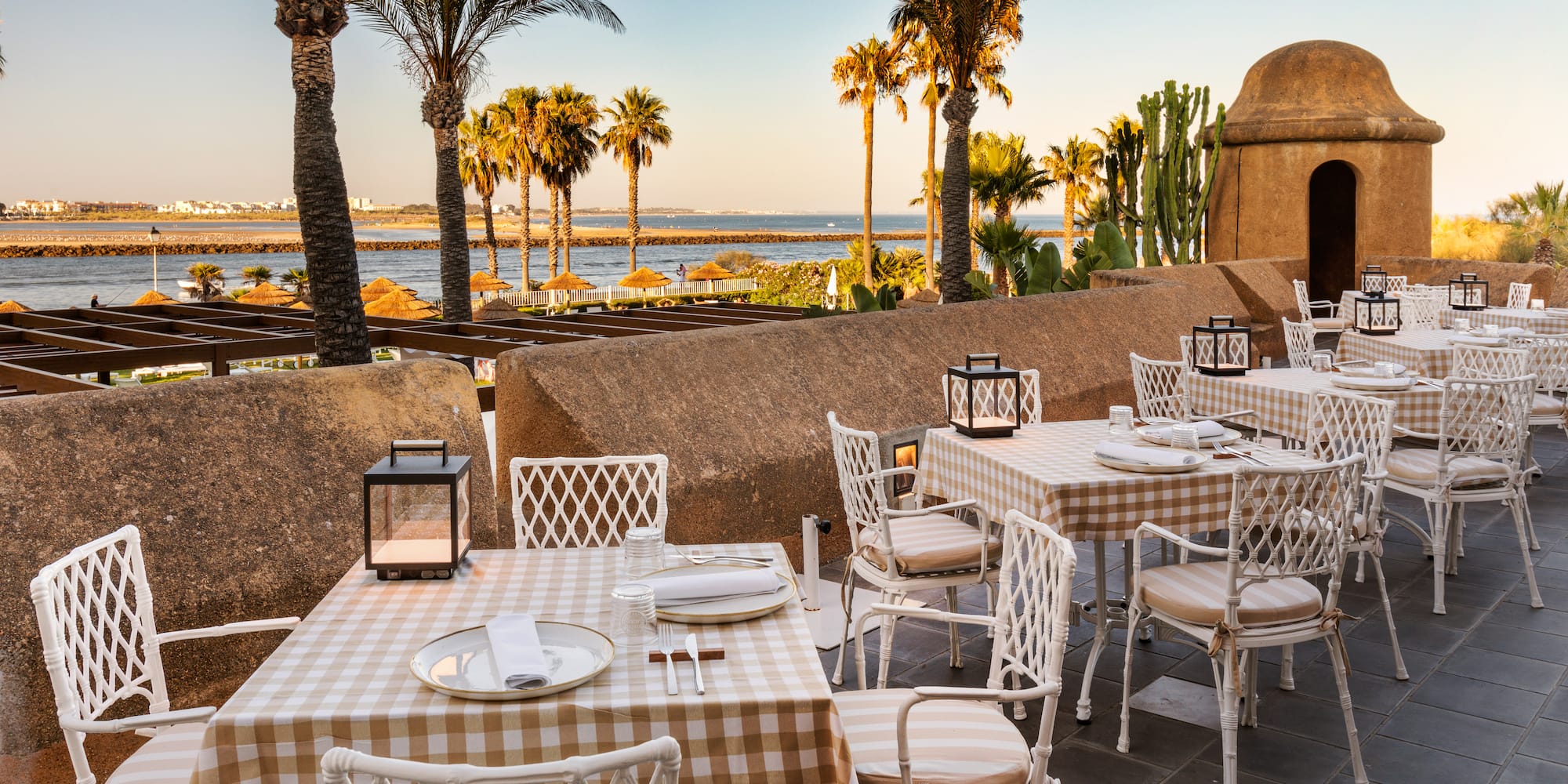 a table and chairs outside with palm trees and water in the background