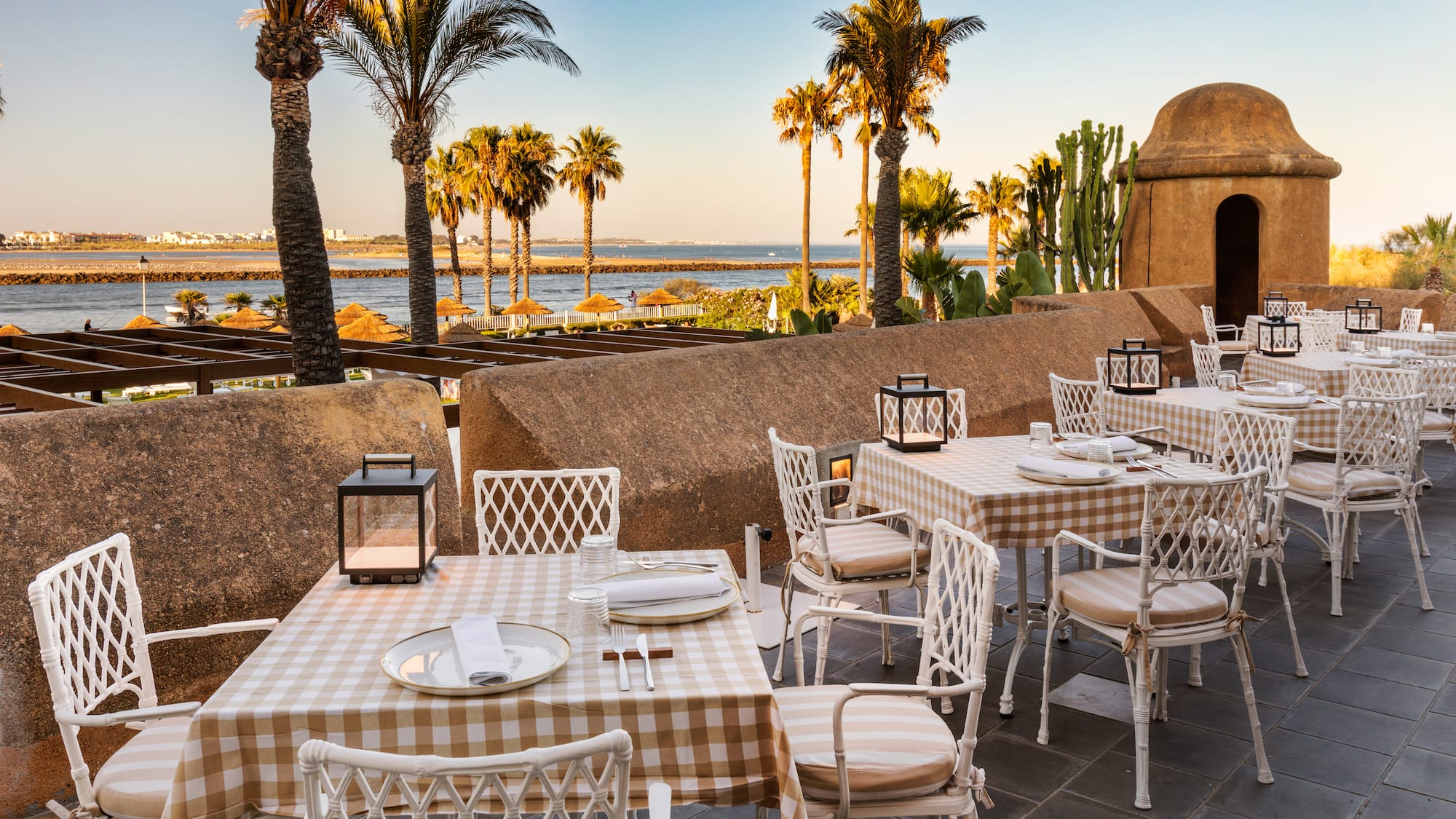a table and chairs outside with palm trees and water in the background