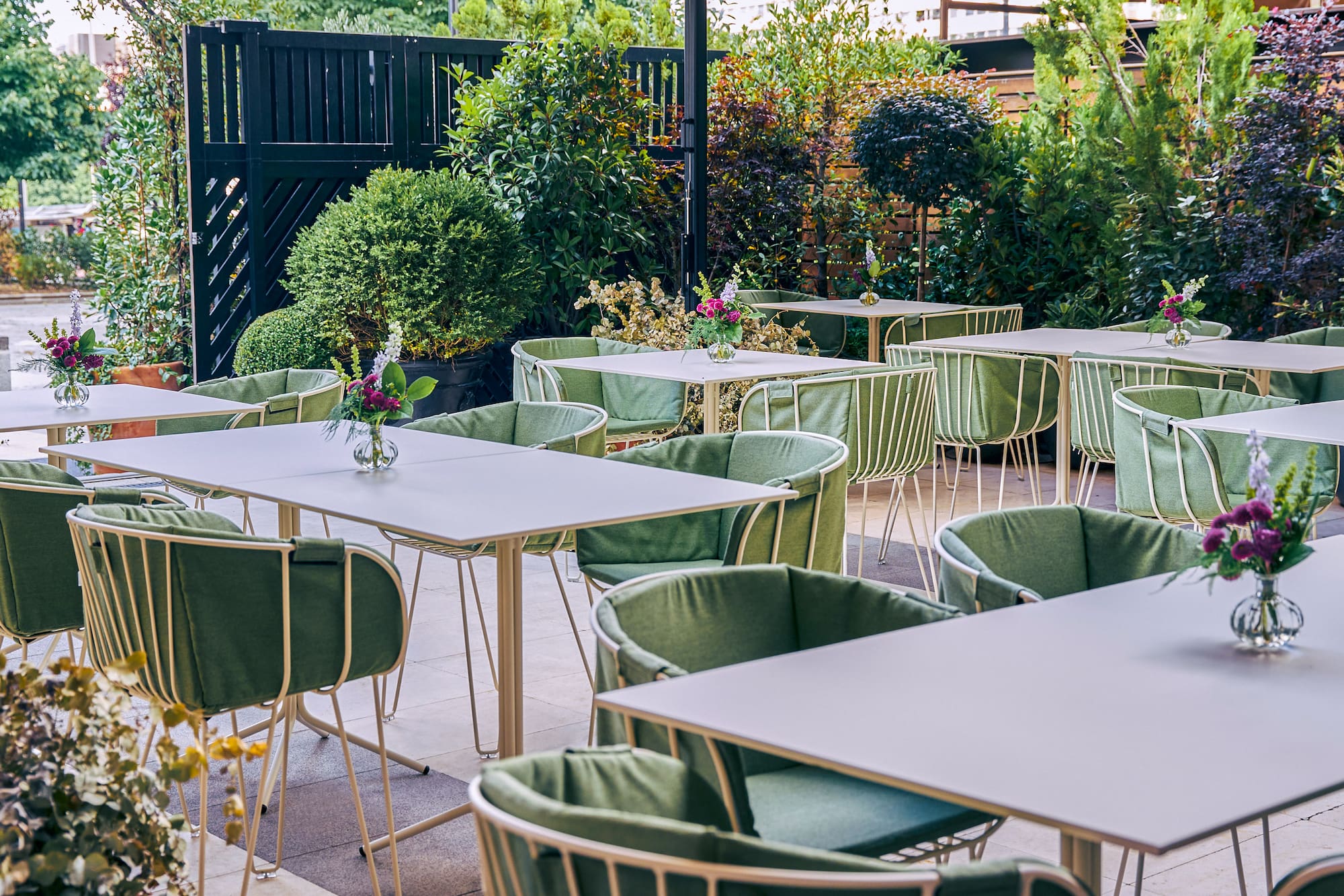 Outdoor restaurant patio with green chairs, white tables, and lush greenery.