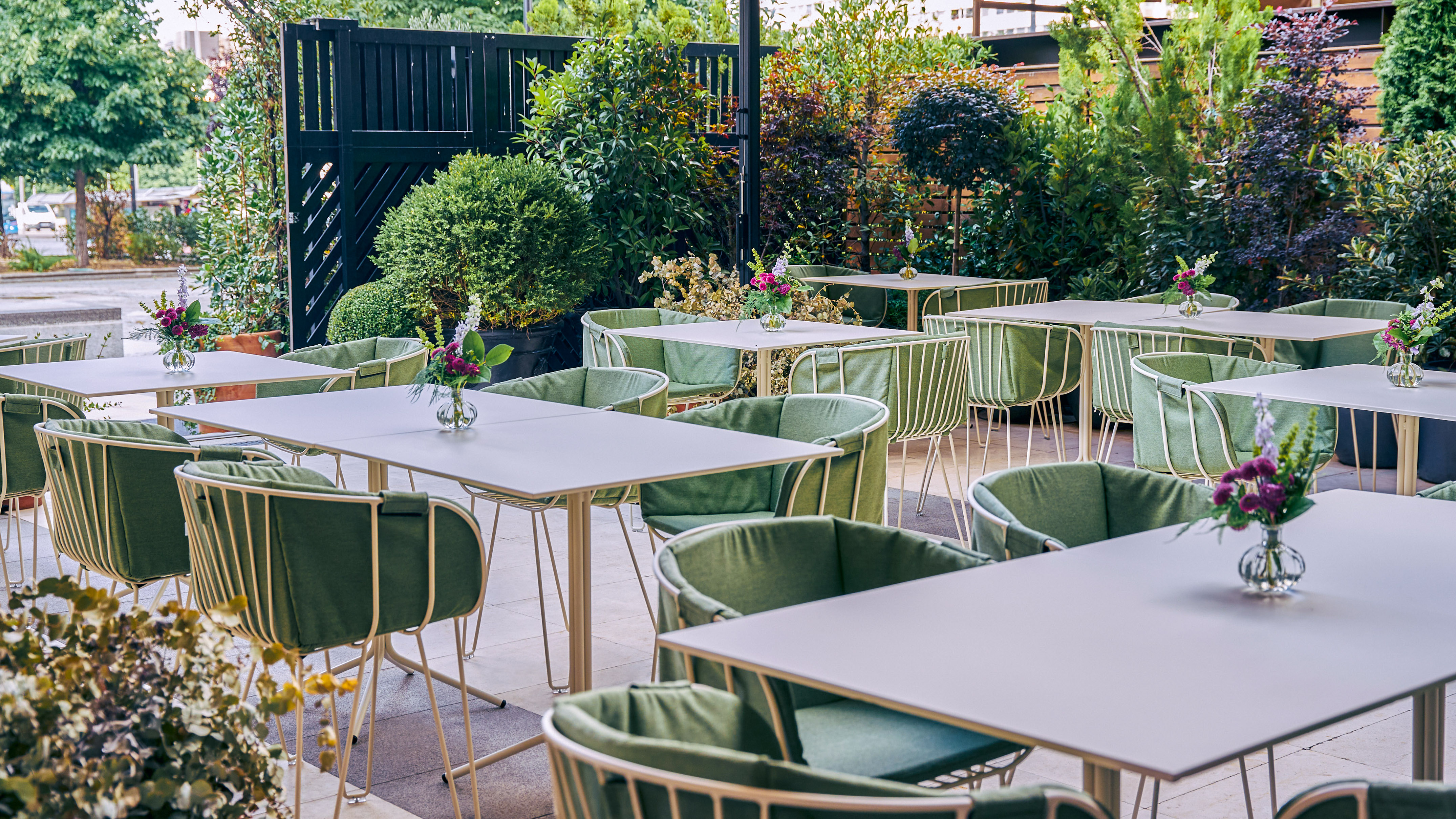 Outdoor restaurant patio with green chairs, white tables, and lush greenery.