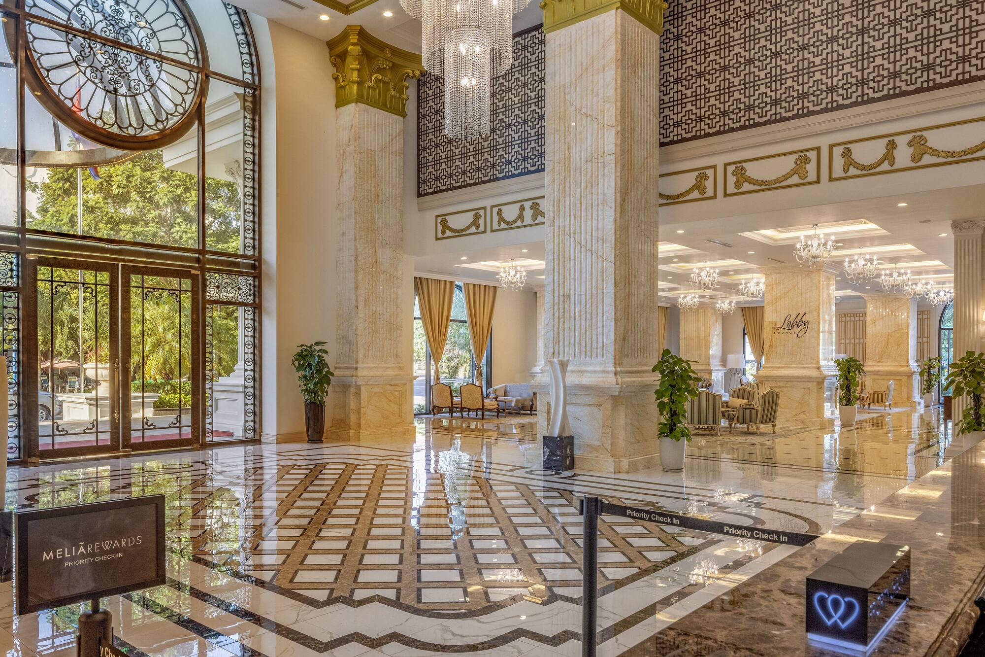 Grand luxury hotel lobby with marble floors, ornate columns, chandeliers, and check-in.