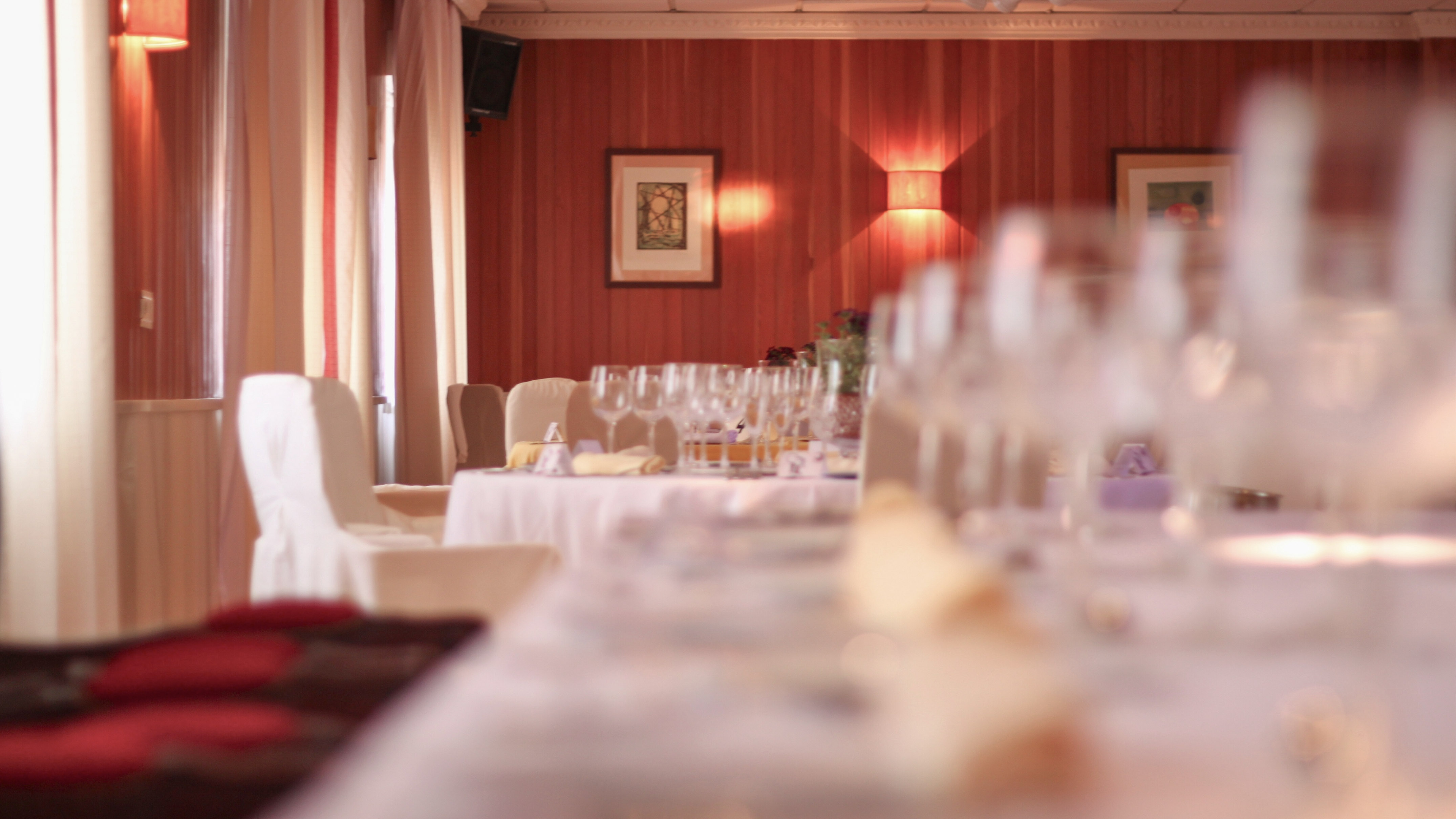 Elegant restaurant dining tables set with wine glasses and warm red walls.