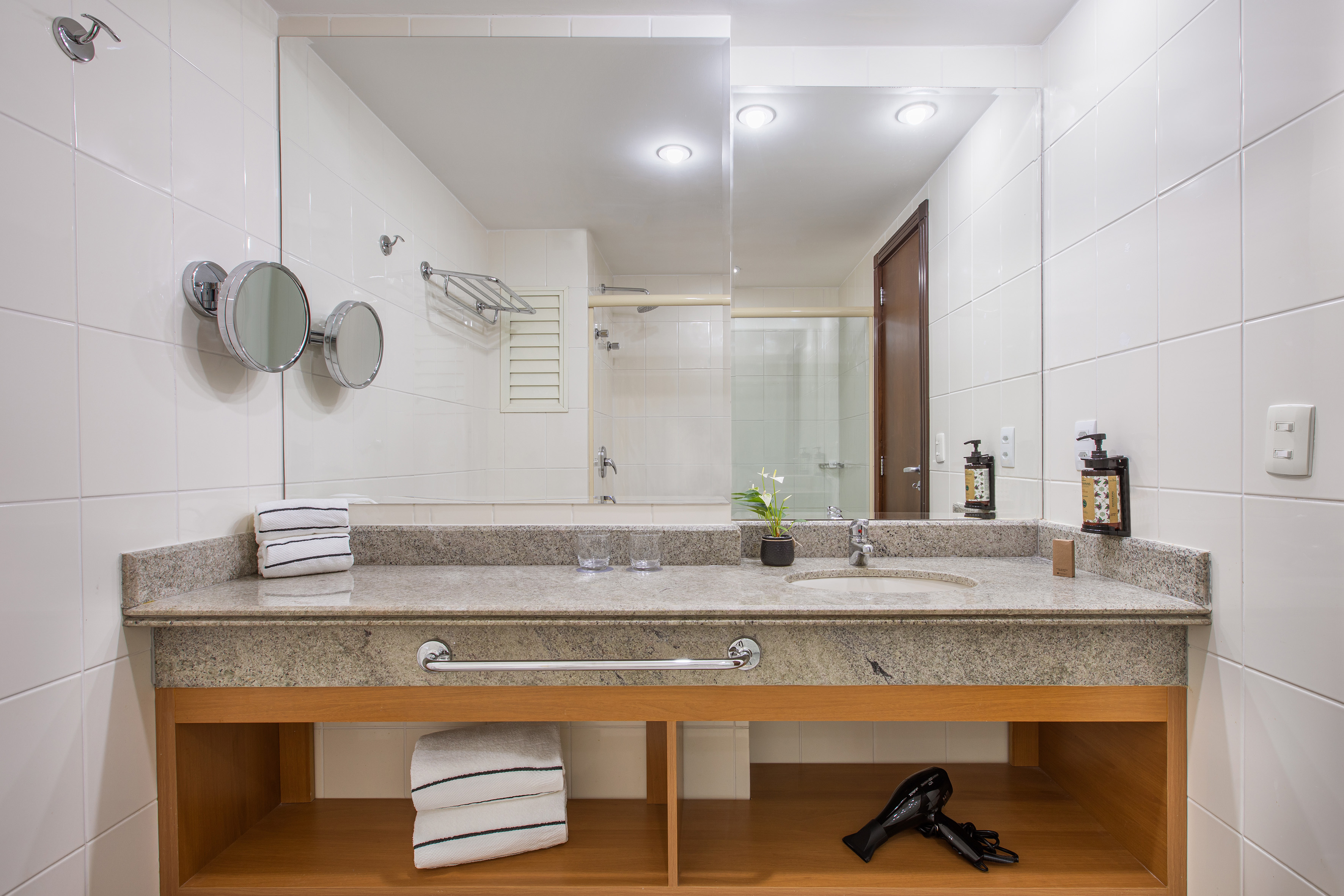 Hotel bathroom vanity, granite countertop, large mirror, white tiled walls.