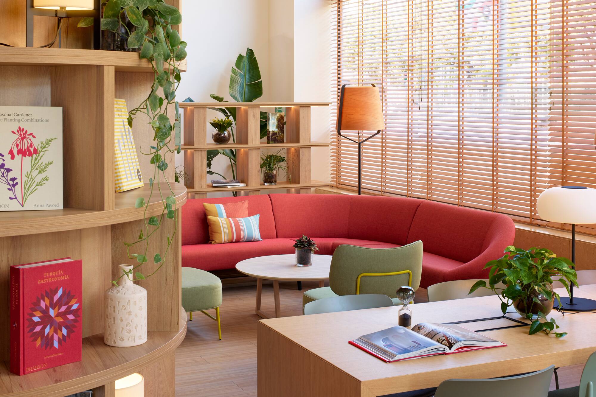 Vibrant lounge with red sofa, wooden decor, green plants, and bright windows.