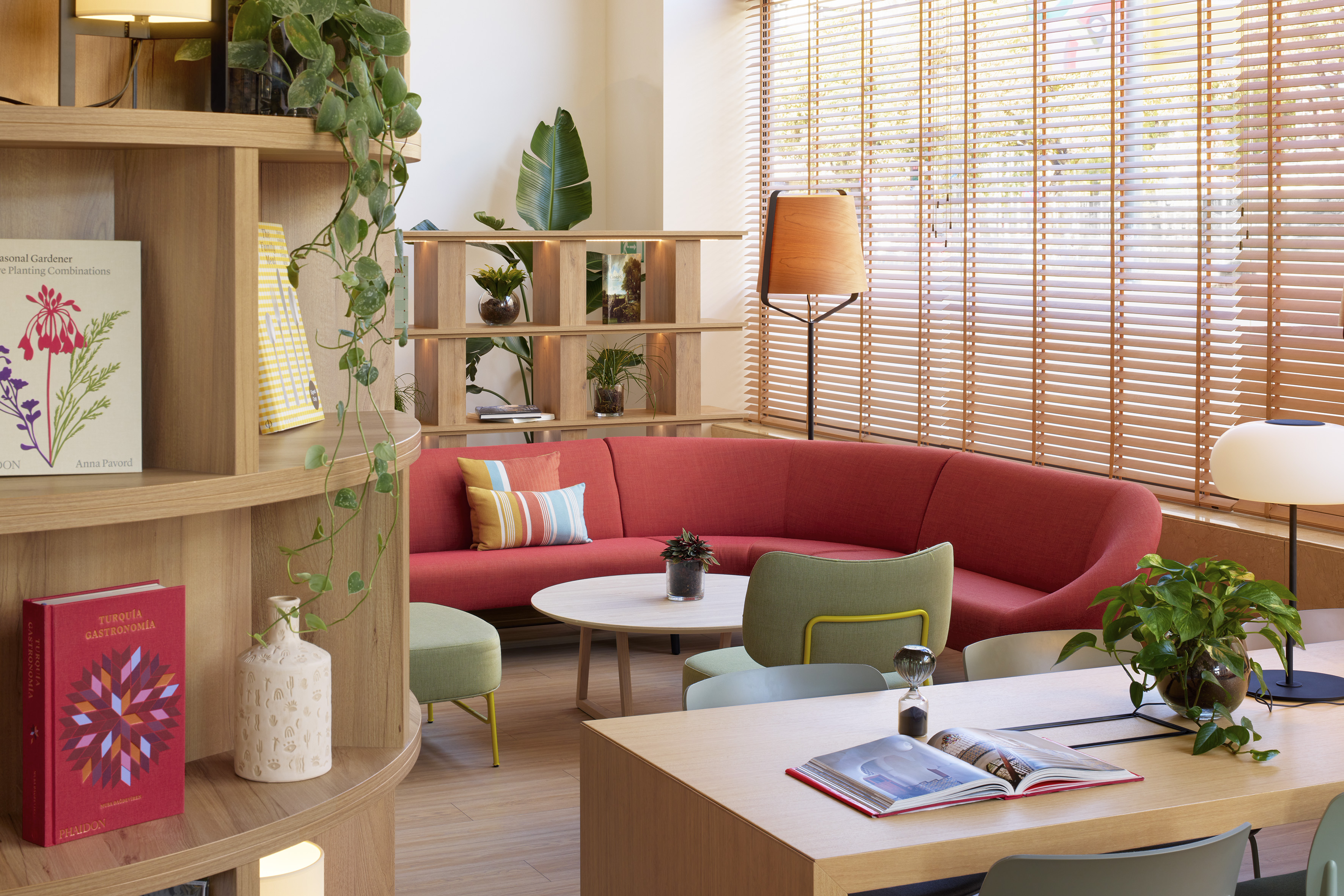 Vibrant lounge with red sofa, wooden decor, green plants, and bright windows.