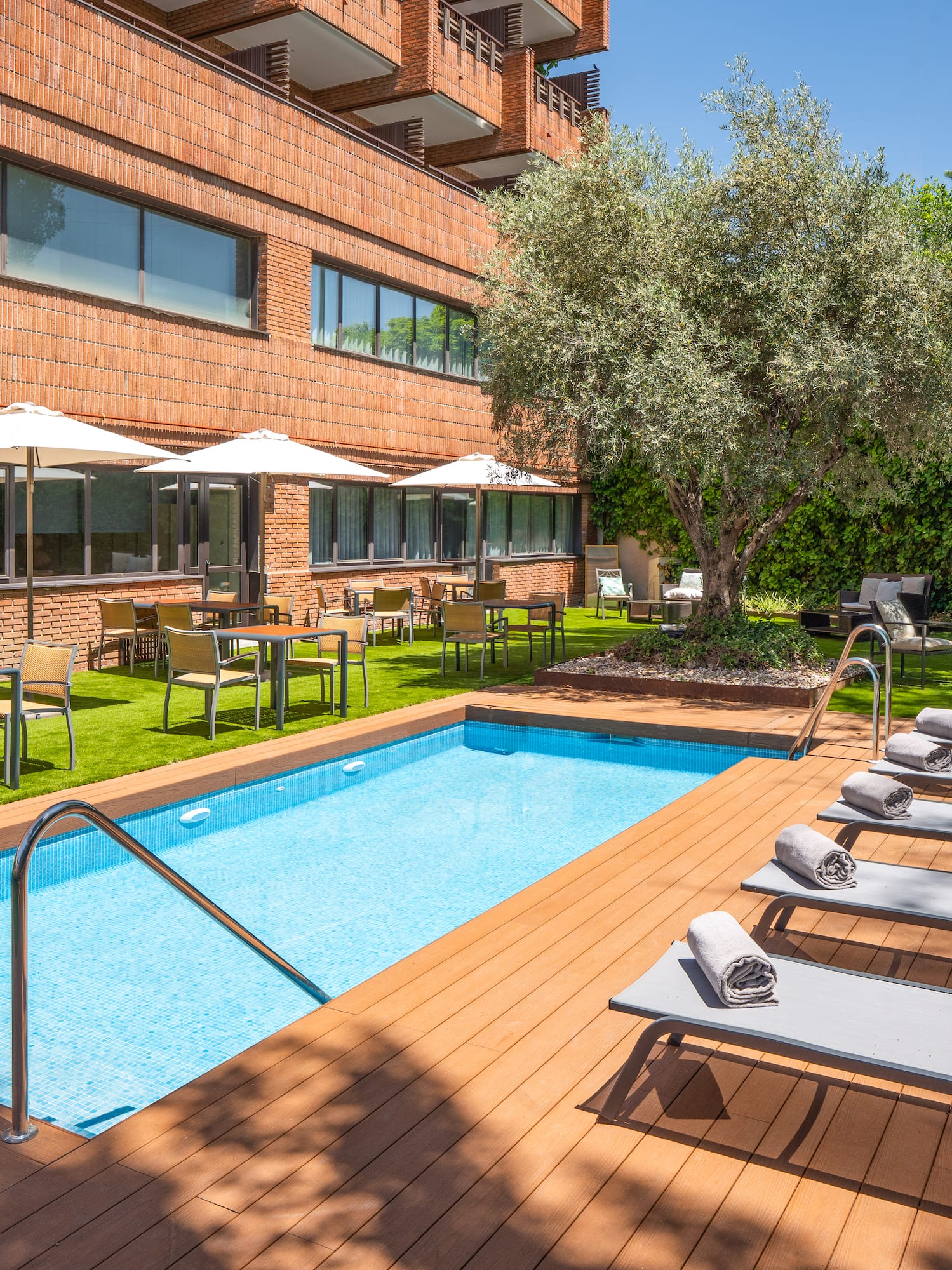 Hotel outdoor swimming pool with loungers, dining, and lush garden.
