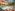 Outdoor hotel swimming pool with wooden deck, sun loungers, and garden dining.