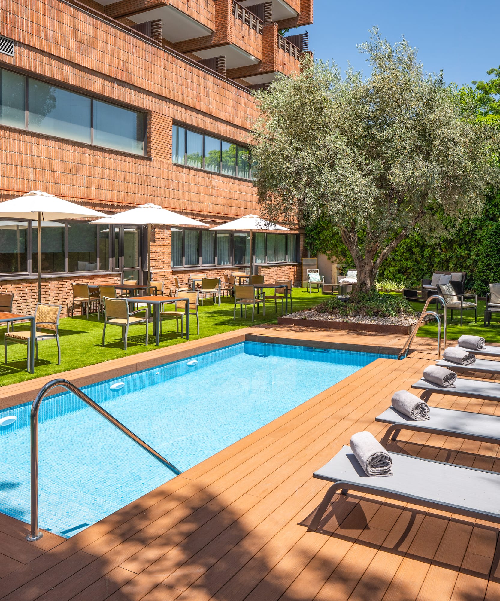 Hotel outdoor swimming pool with loungers, dining, and lush garden.