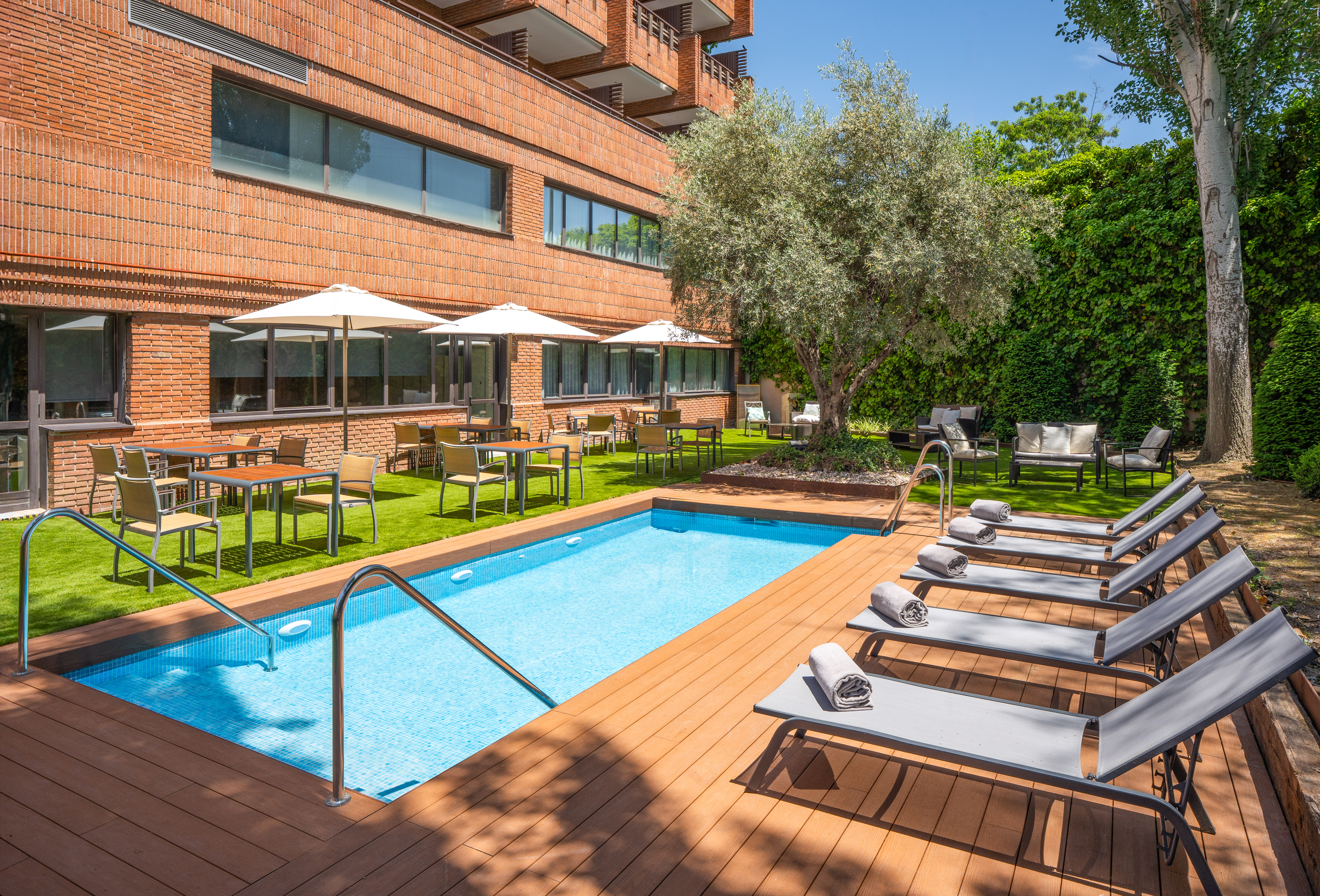 Hotel outdoor swimming pool with loungers, dining, and lush garden.