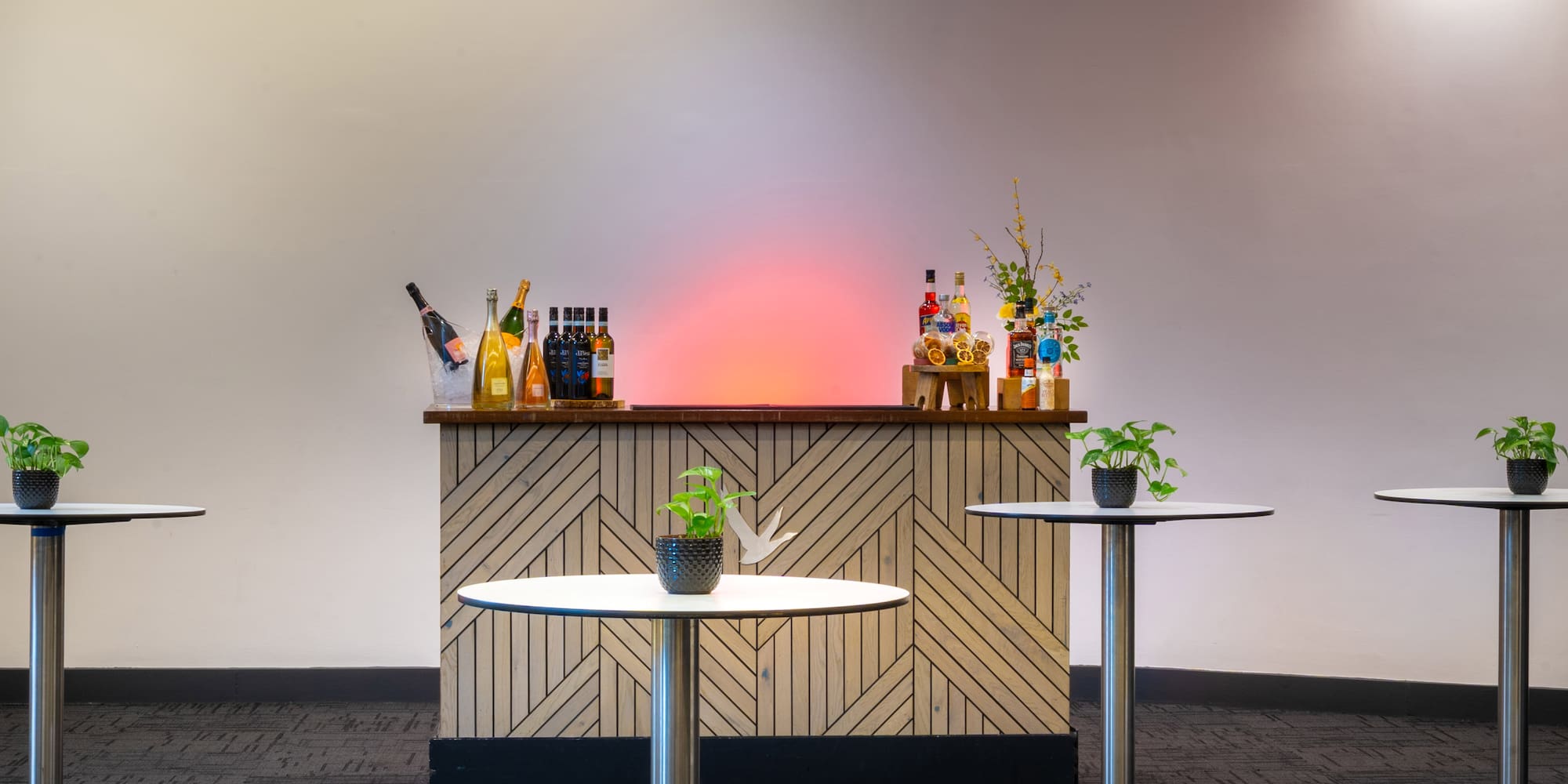 Modern event bar with drinks, high-top tables, and glowing wall for reception.