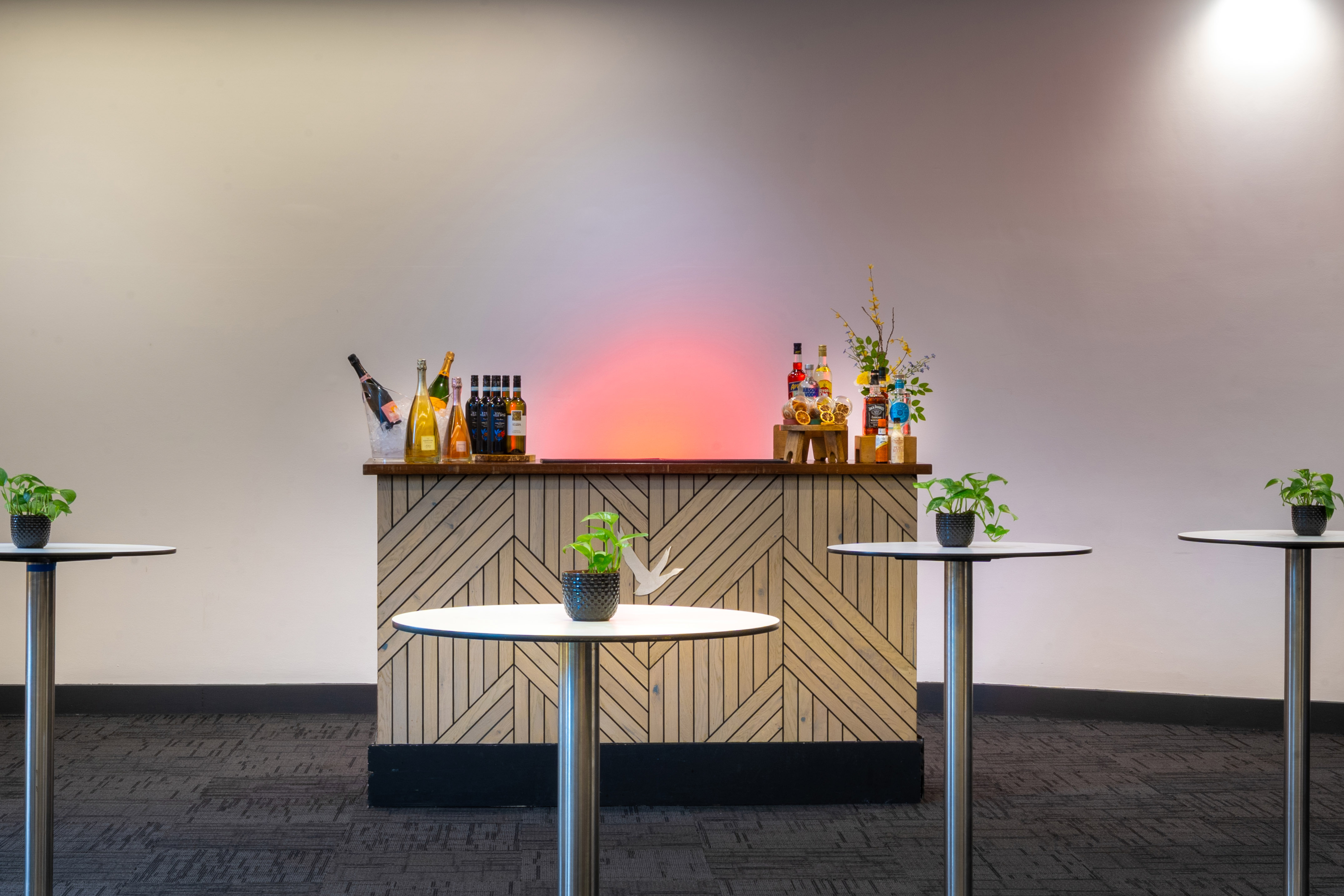 Modern event bar with drinks, high-top tables, and glowing wall for reception.